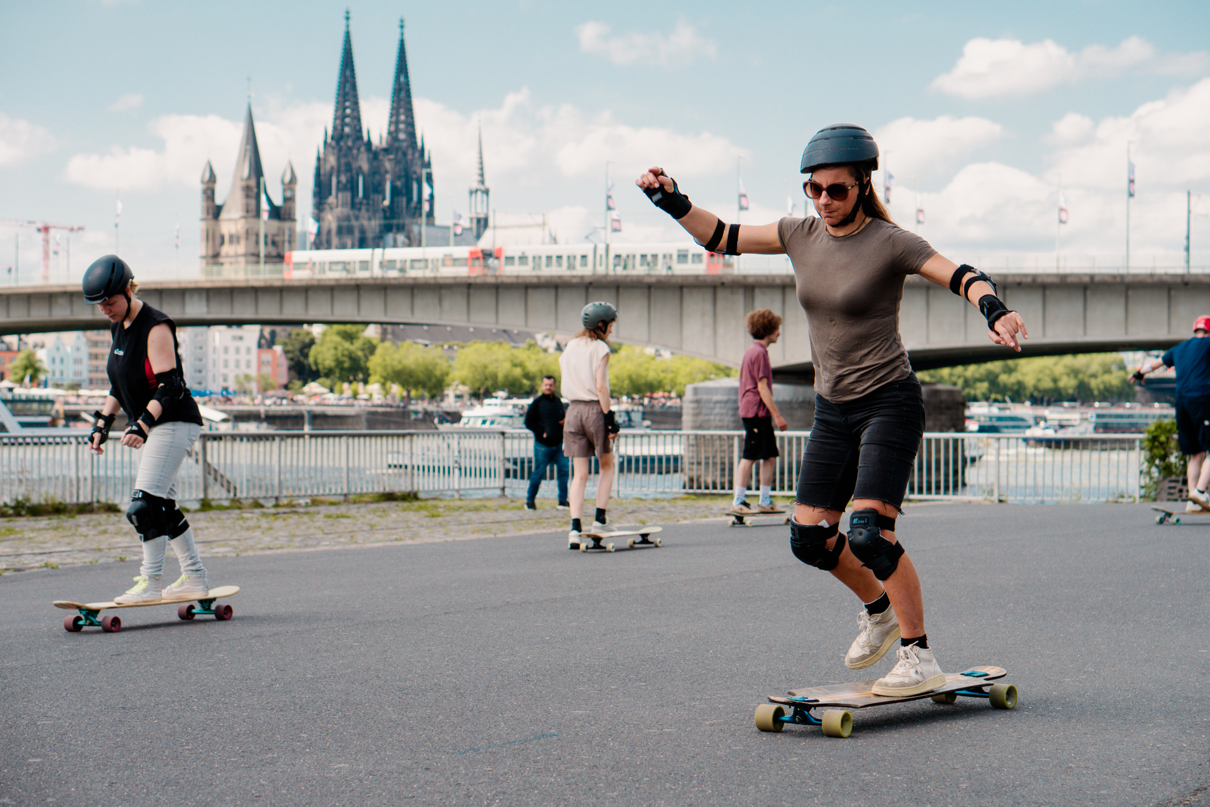Menschen fahren Skateboard nahe einem Fluss mit Brücke.