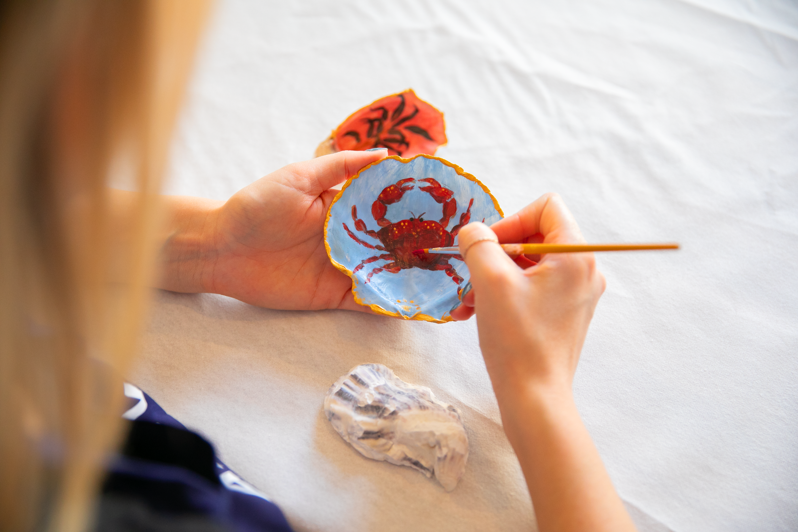 Person painting crab on shell indoors.