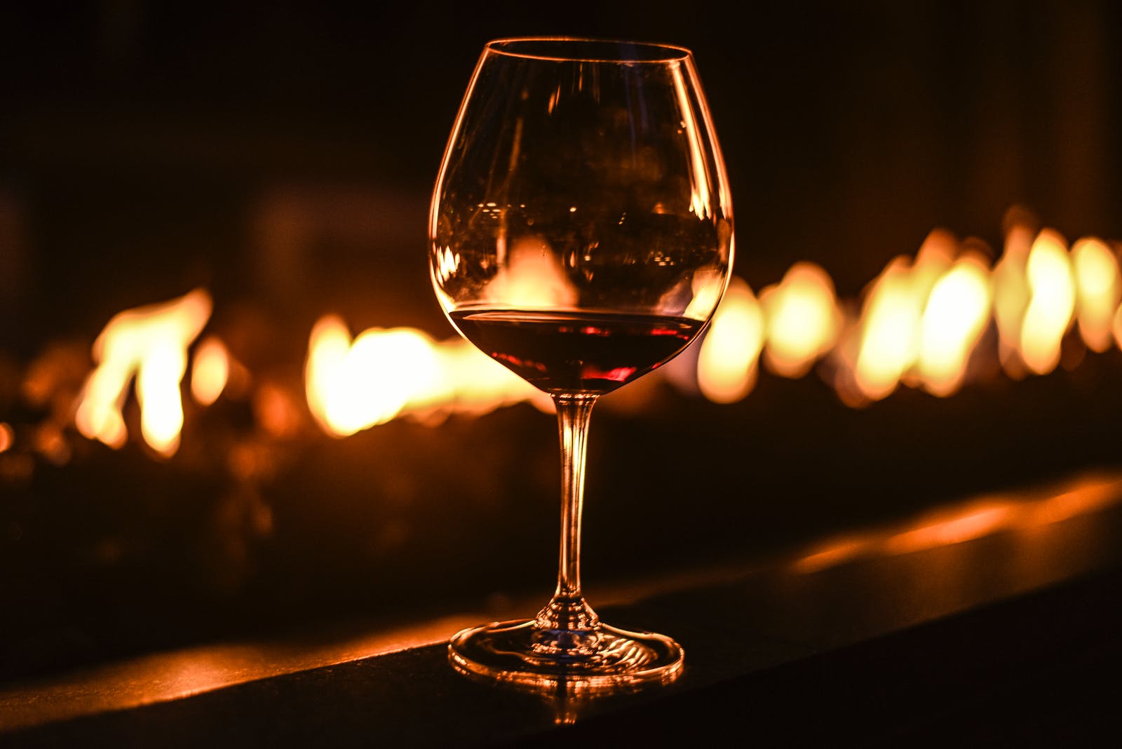 Rotwein-Glas steht vor einem flackernden Feuer.