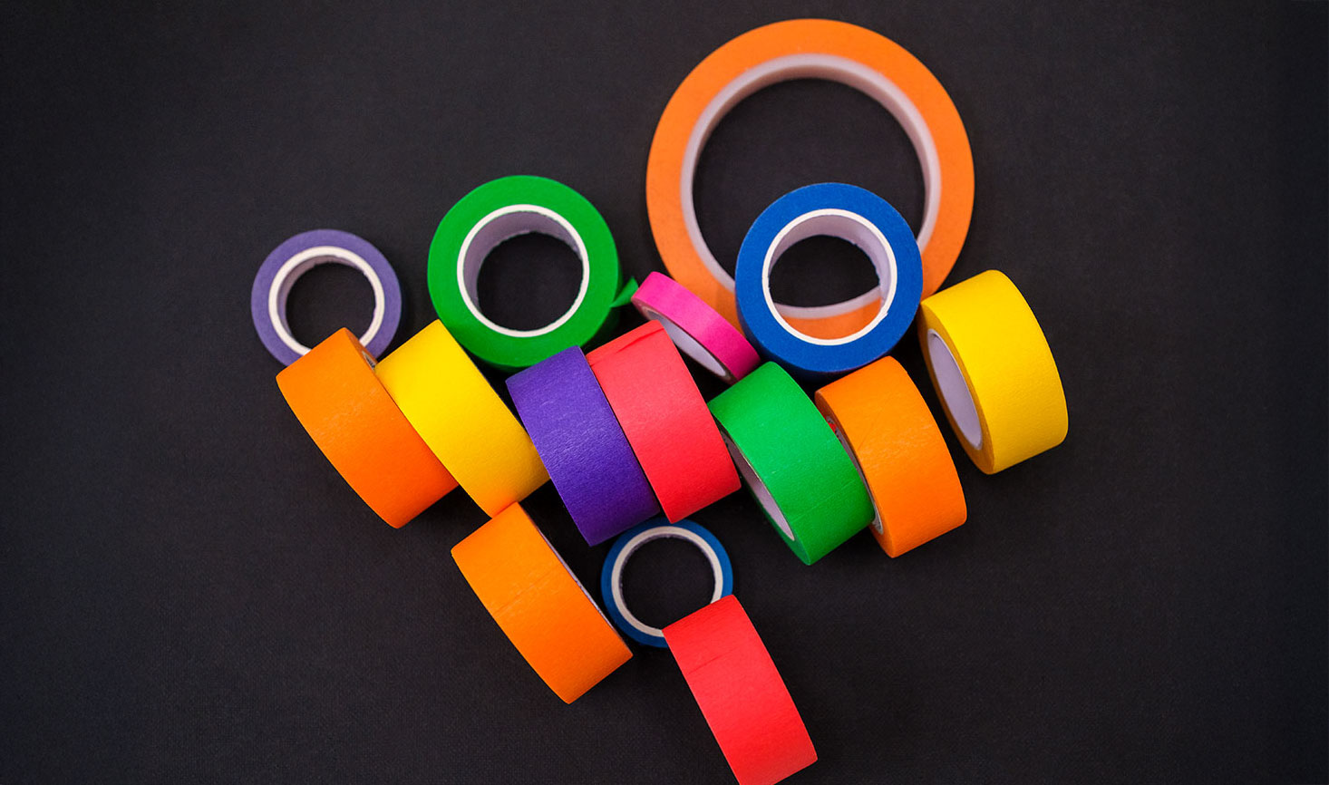 Colorful tape rolls scattered on black background.