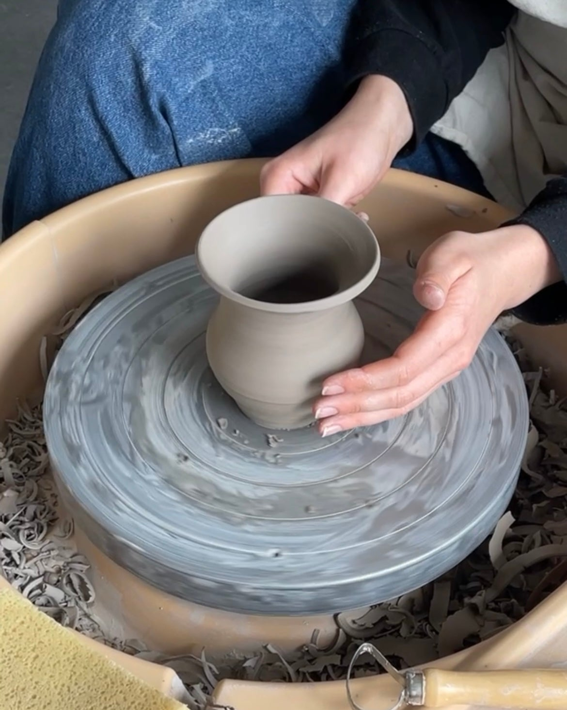 Hands shaping pottery on a spinning wheel.