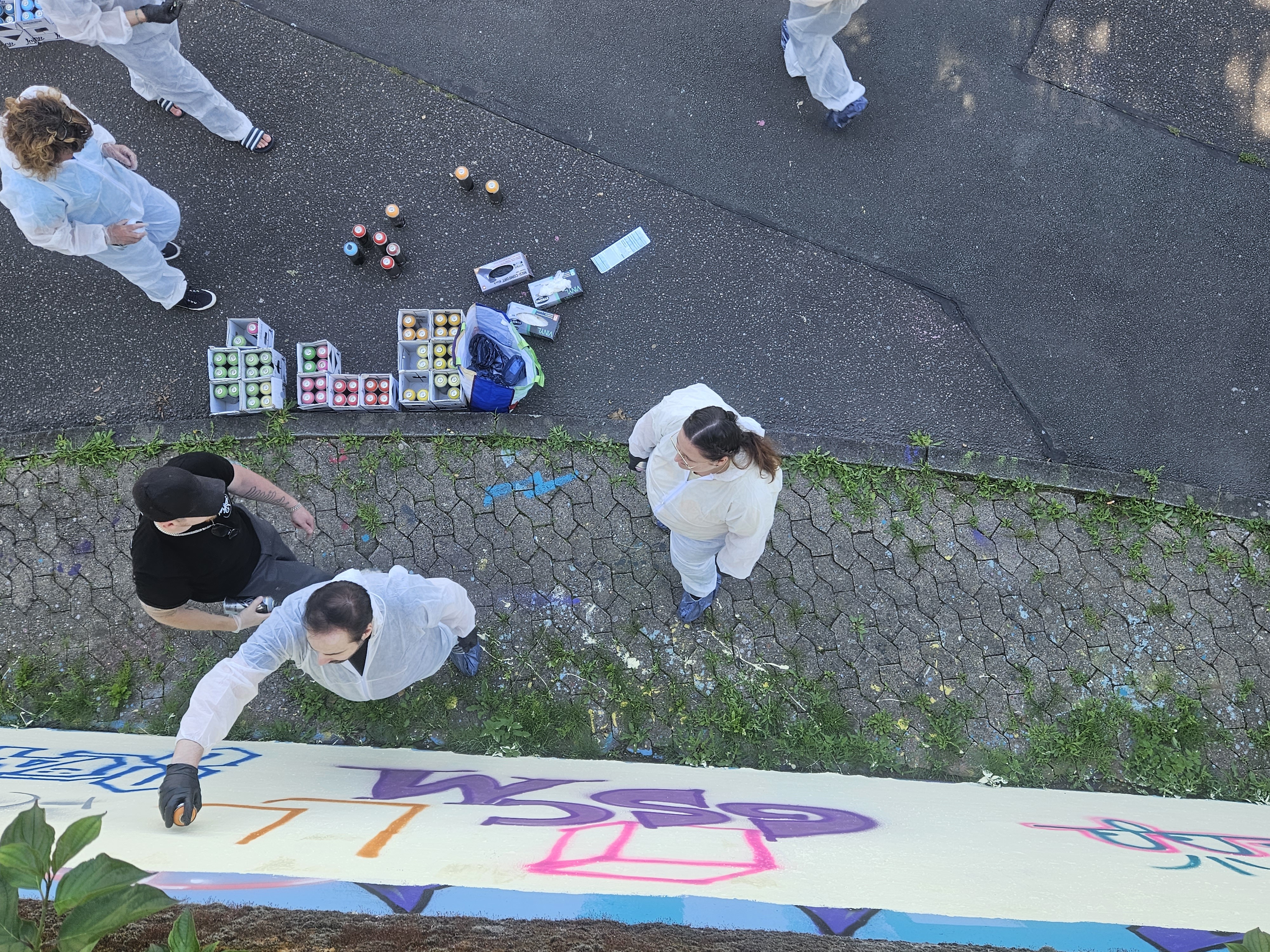 Menschen malen Graffiti an einer Wand draußen.