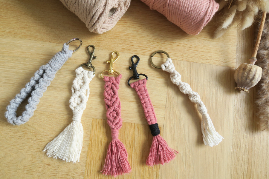 Five macrame keychains on wooden surface.