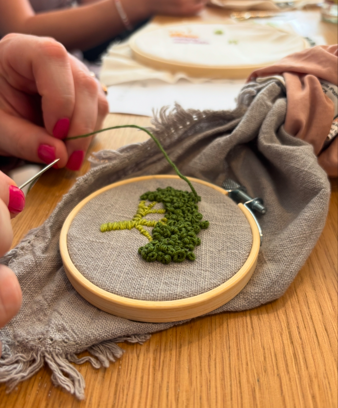 Hands embroidering green design on wooden hoop.