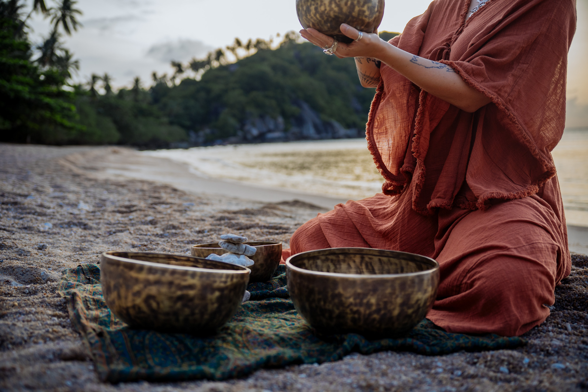 Woman playing singing bowls on beach.