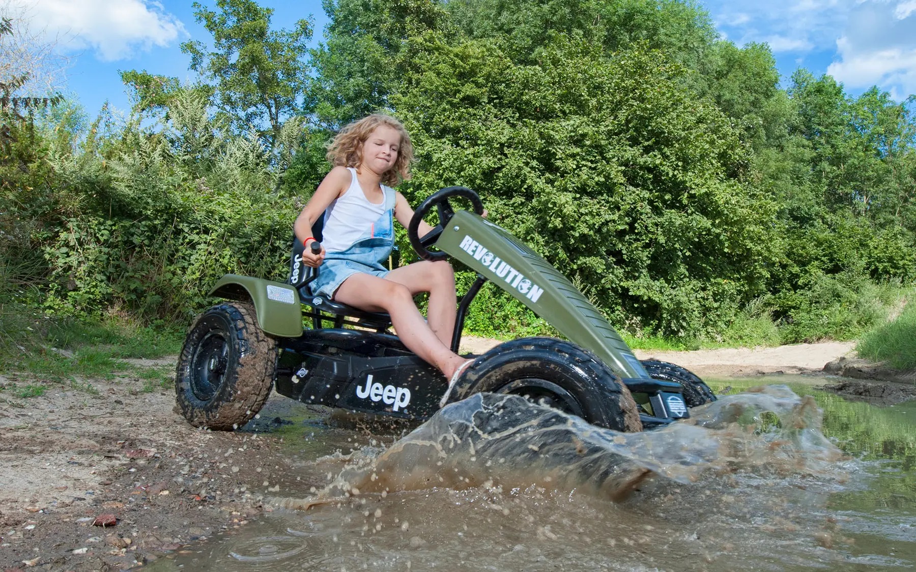 Child driving go-kart splashing through mud.