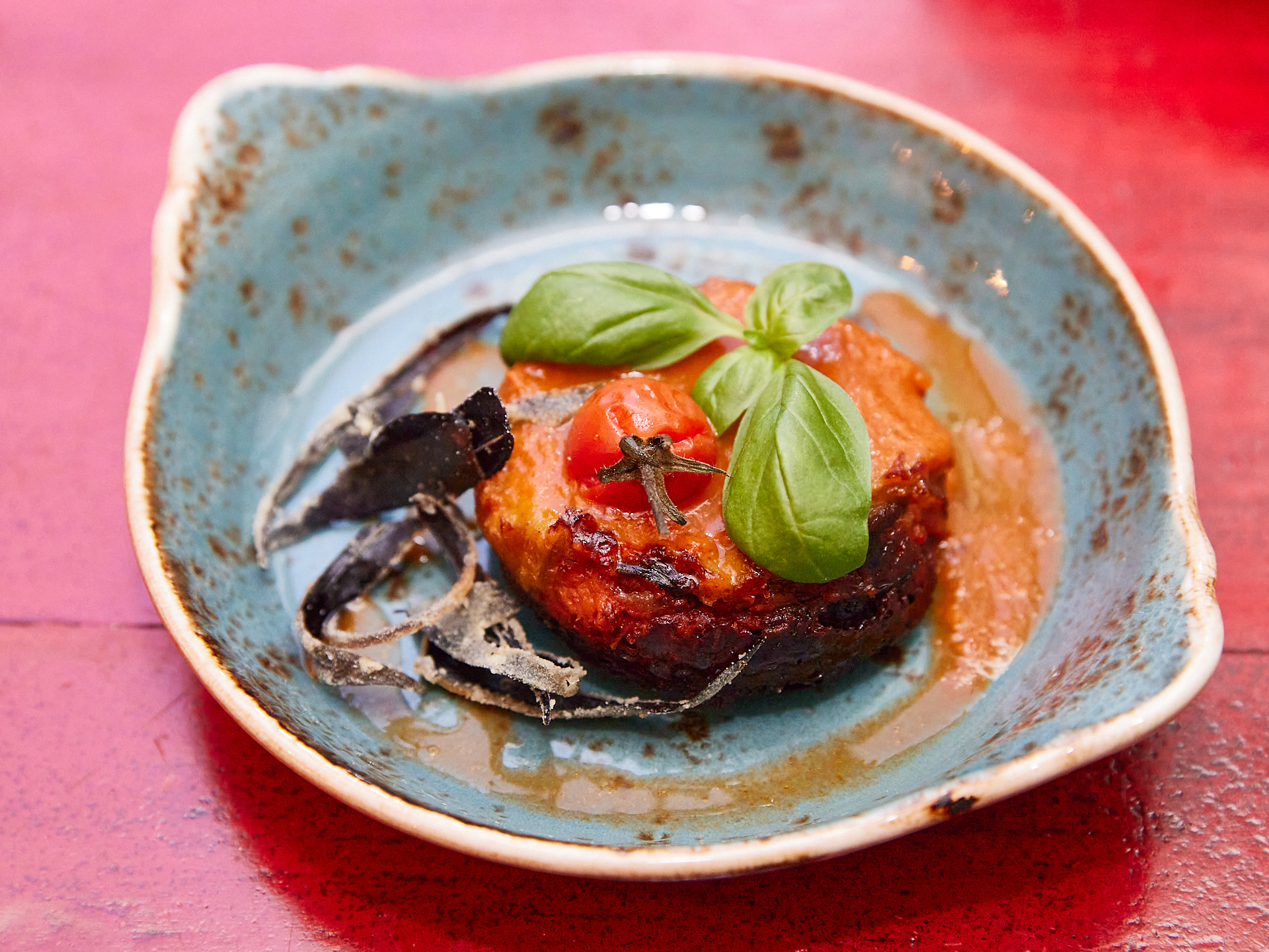Gourmetgericht mit Tomate, Basilikum-Garnitur, türkisfarbener Teller.