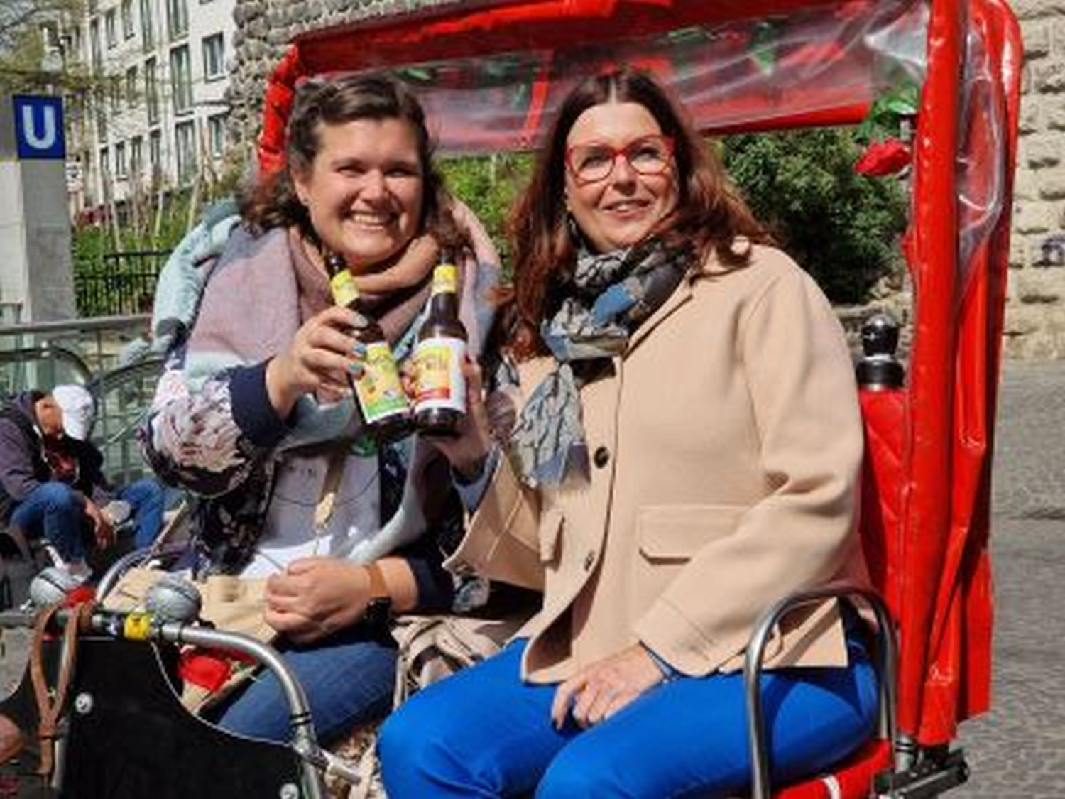 Two women sitting, holding bottles, outdoors.
