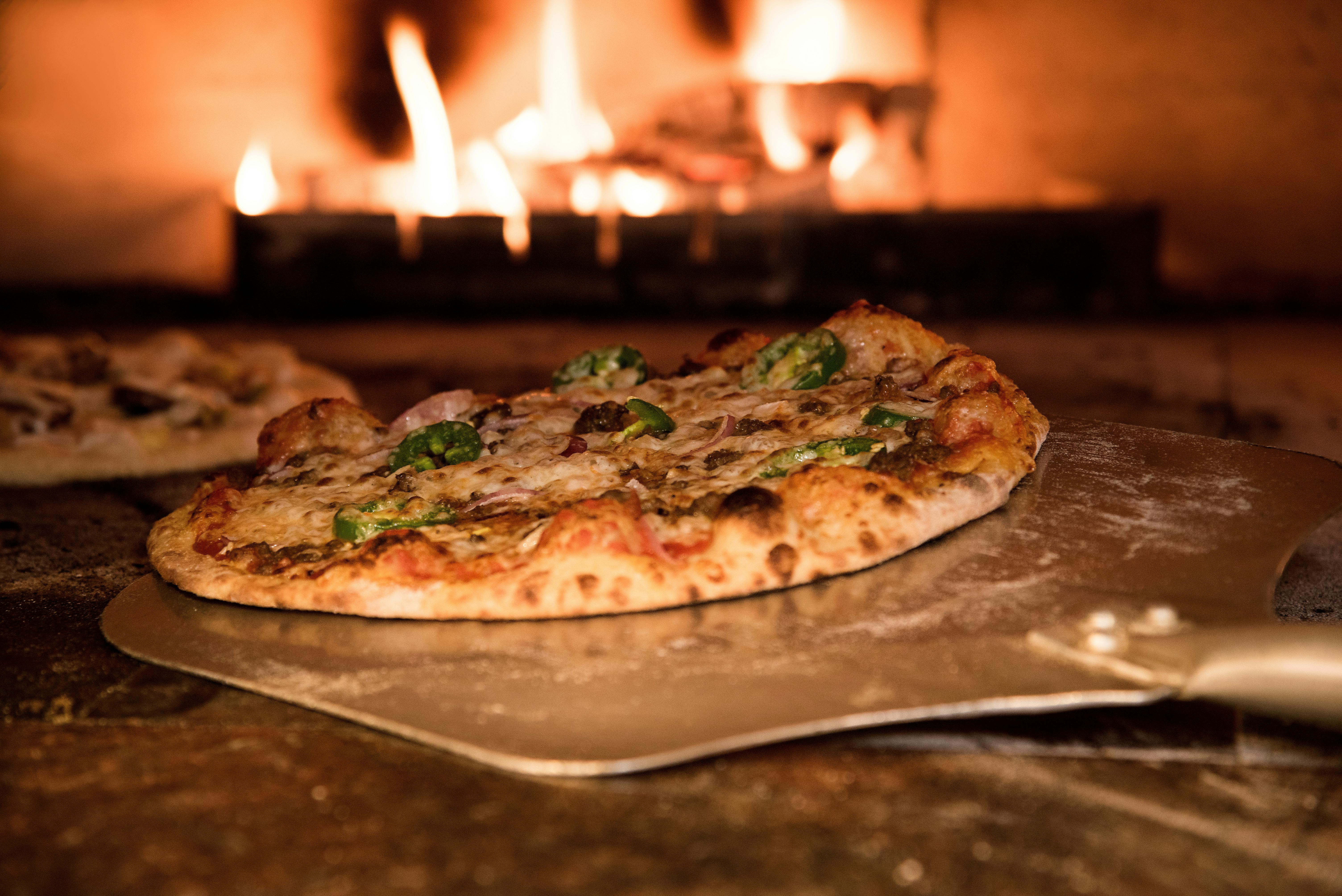 Pizza on peel in front of wood-fired oven.