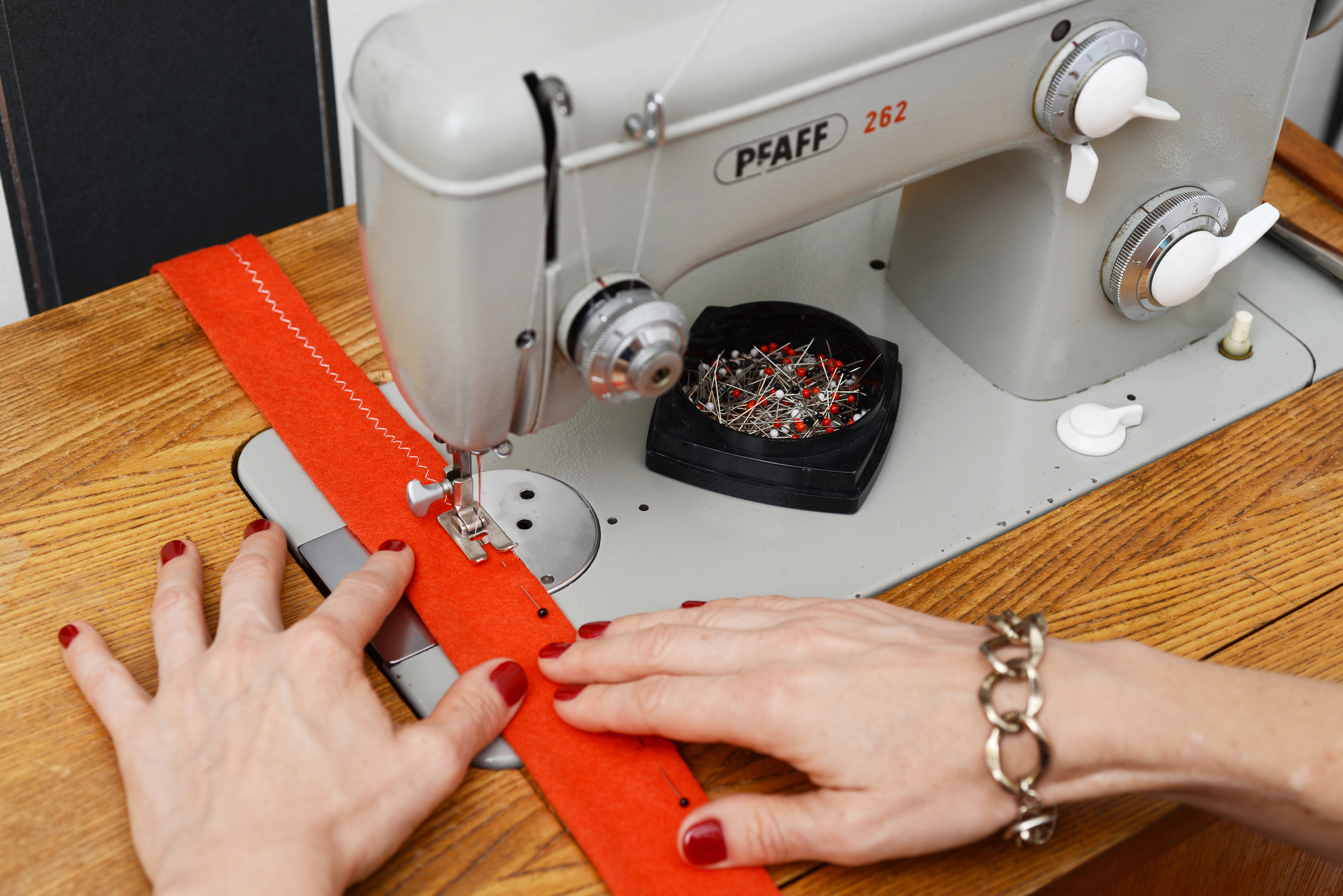 Hands sewing red fabric on Pfaff machine.