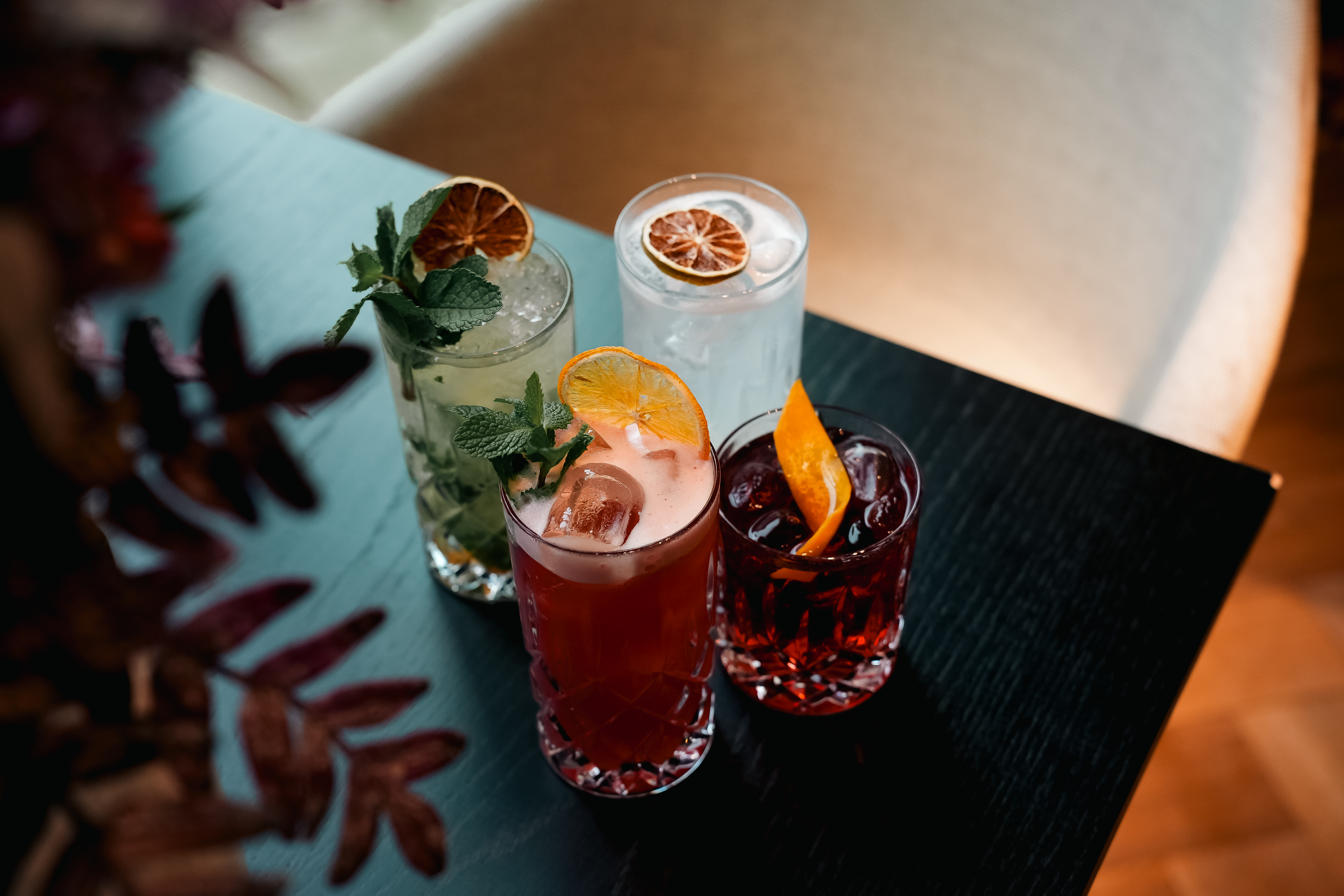 Vier bunte Cocktails auf einem dunklen Tisch.