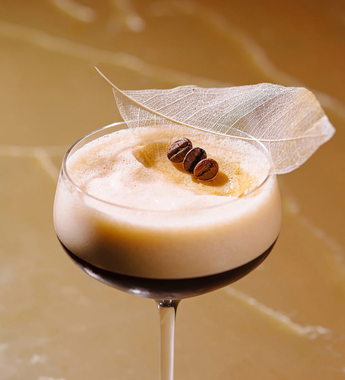 Coffee cocktail with beans and leaf garnish.