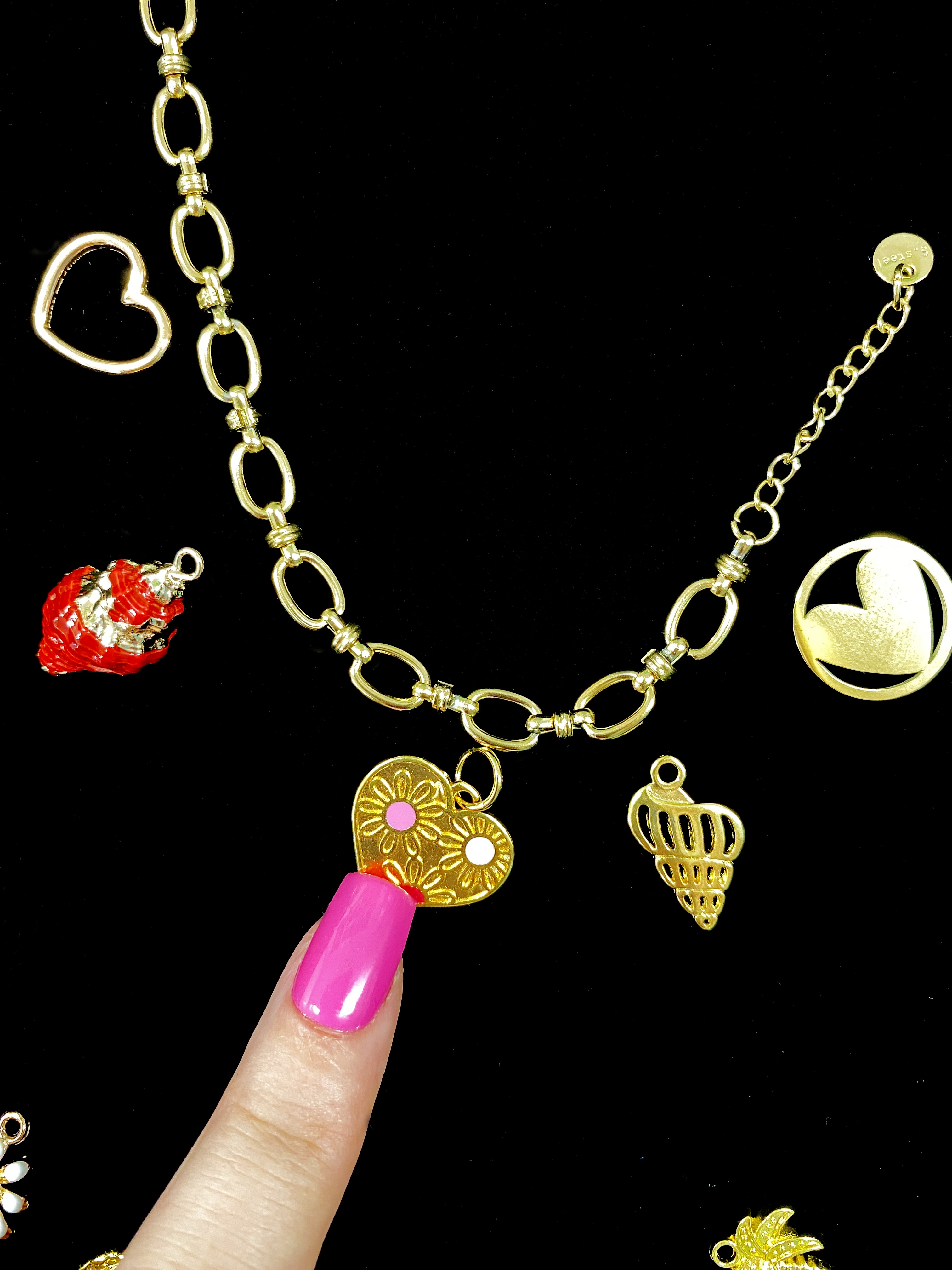 Gold heart charms on a chain with finger.