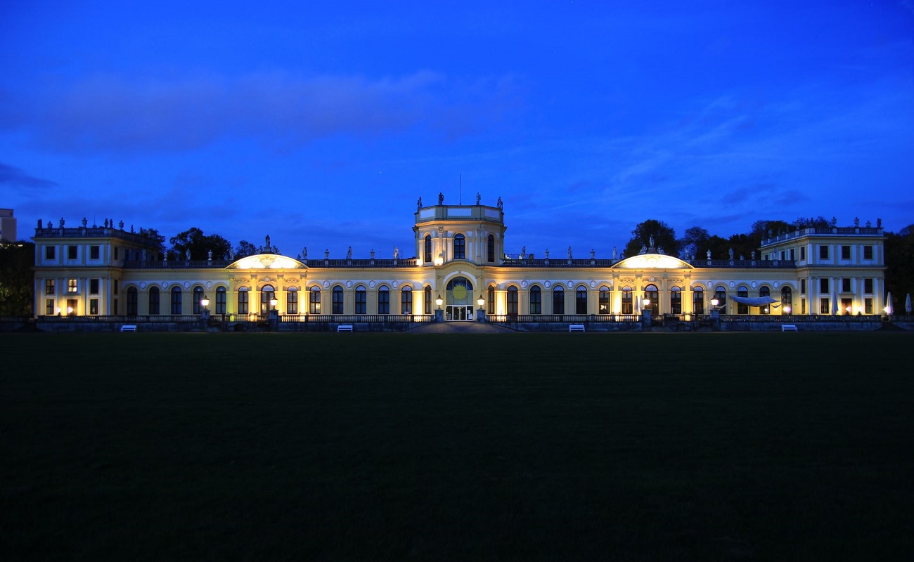 Historisches Gebäude leuchtet nachts, umgeben von Grünflächen.