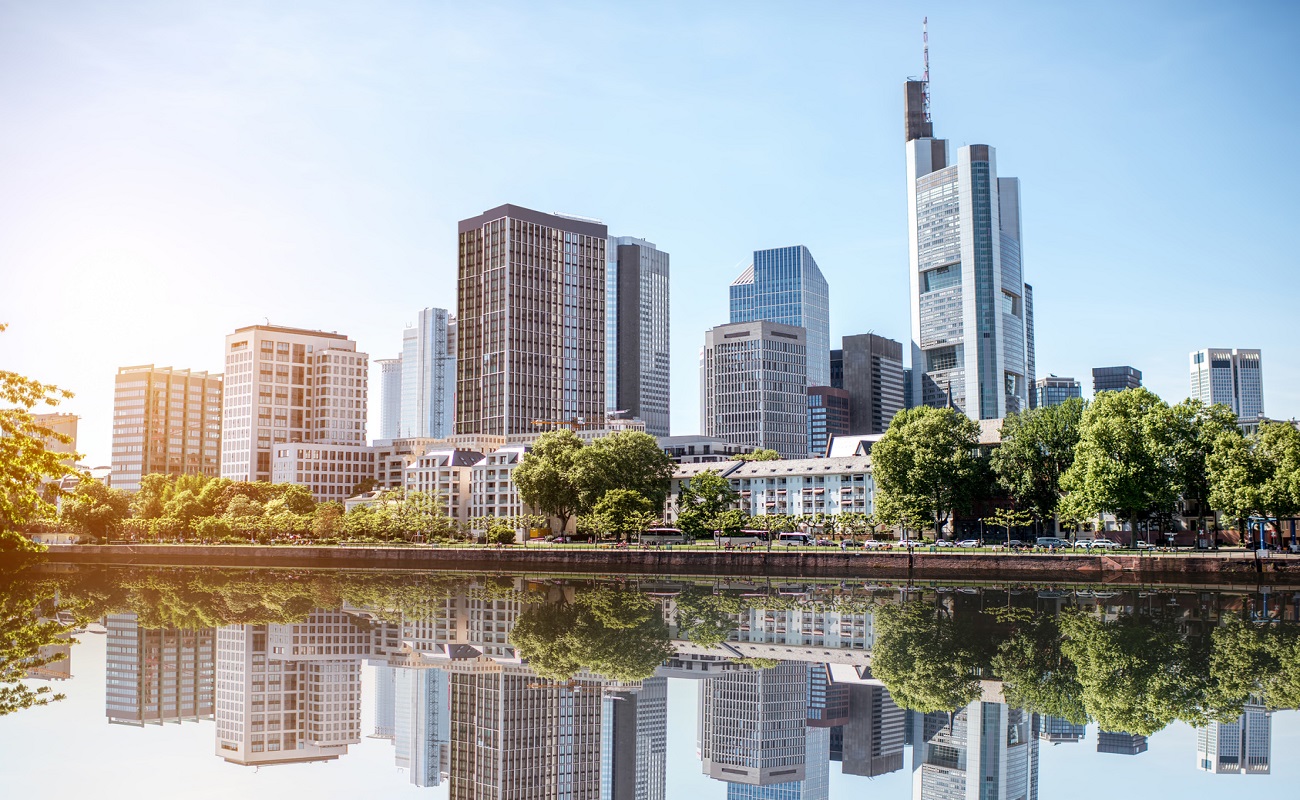 Hochhäuser reflektieren im ruhigen Wasser eines Flusses.