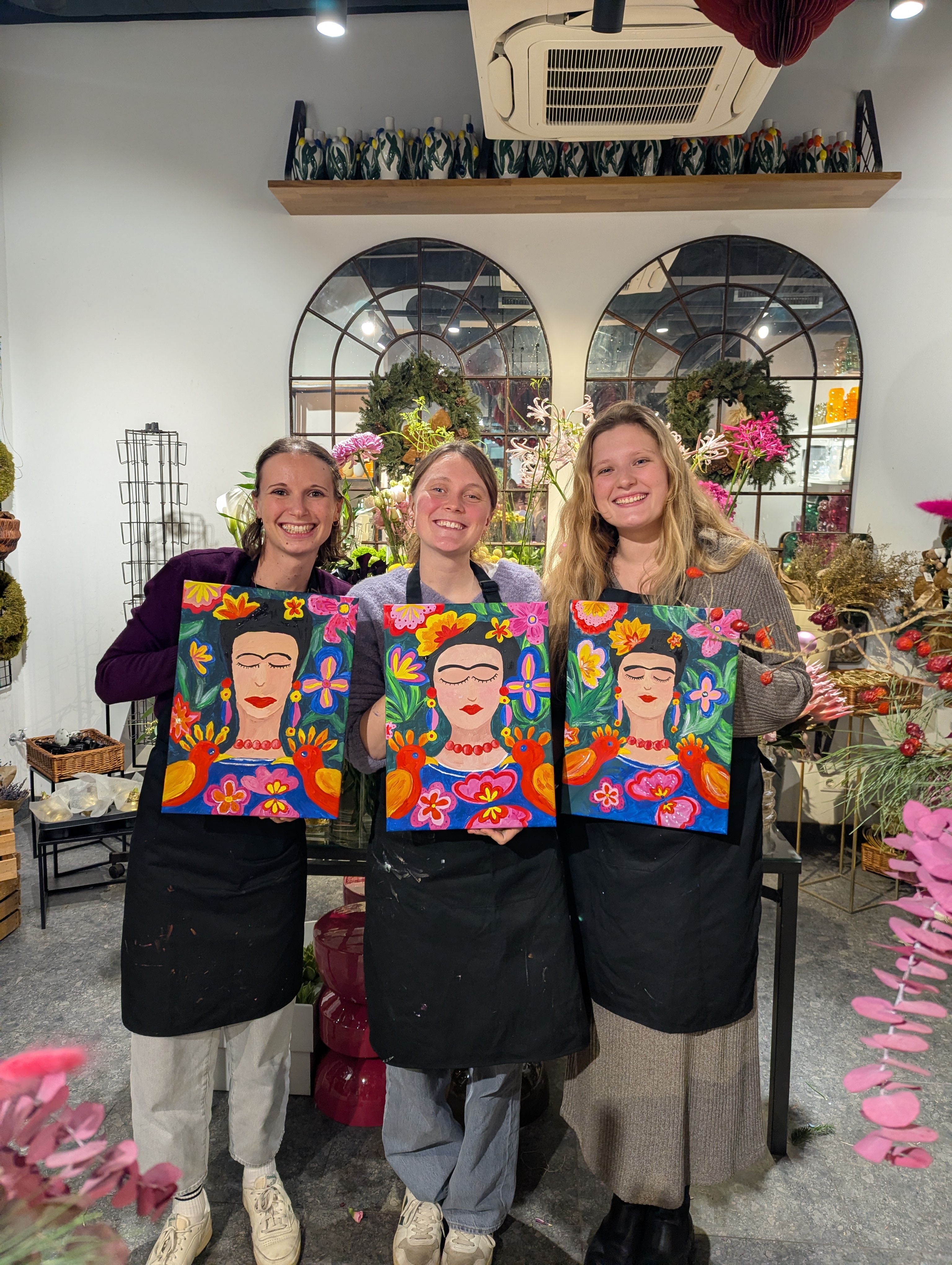 Drei Frauen halten bunte Frida Kahlo Gemälde drinnen.