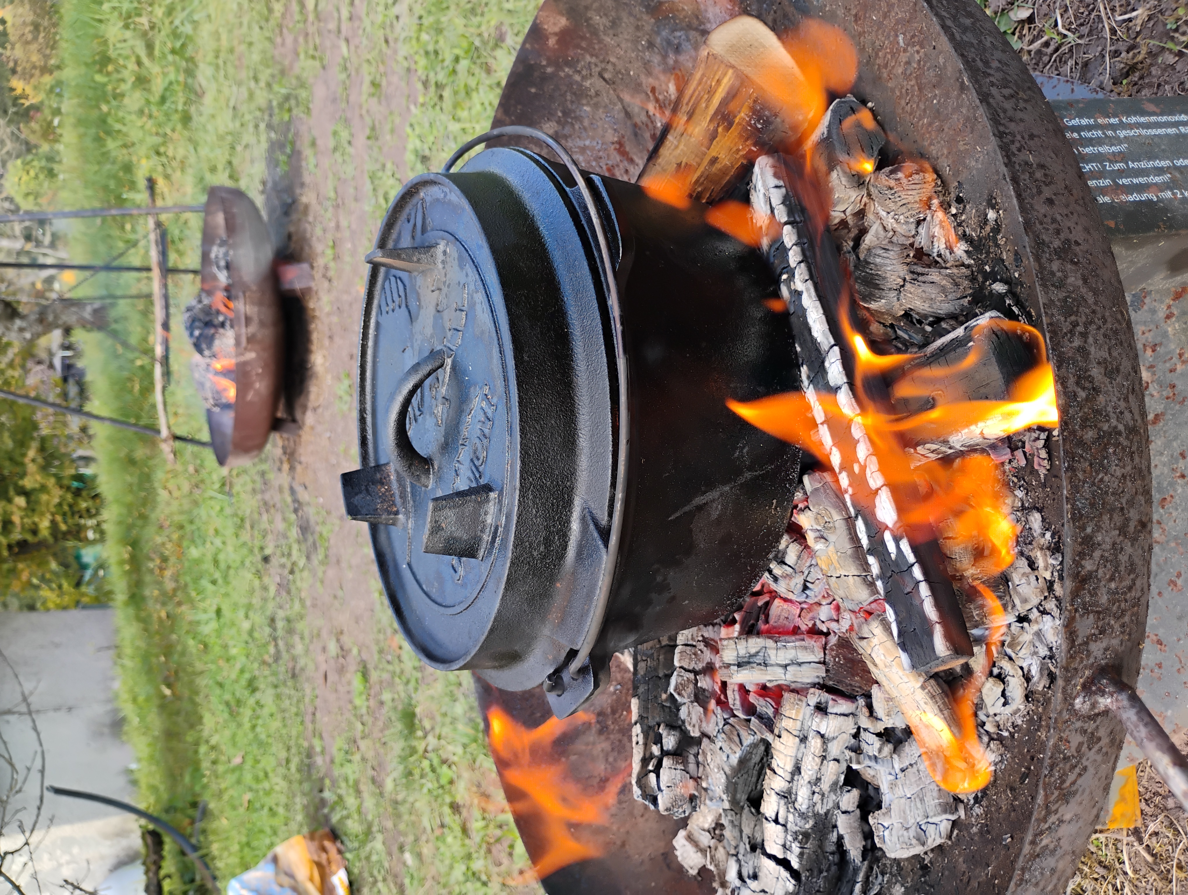 Cast iron pot heated over open fire outdoors.