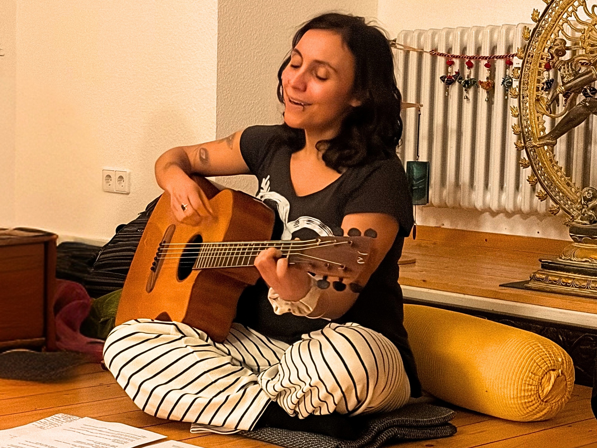 Woman playing guitar, sitting on the floor.