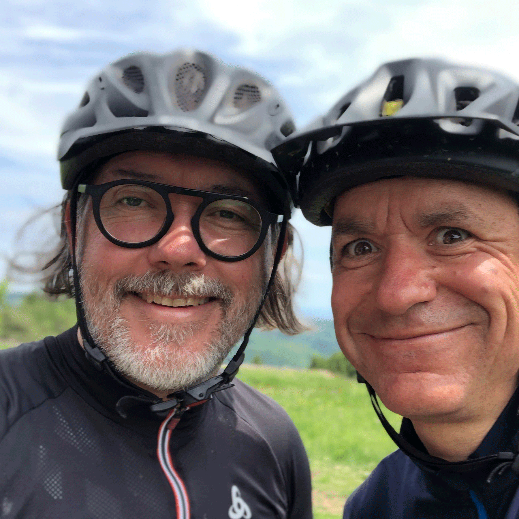 Zwei Radfahrer lächeln mit Helmen im Freien.