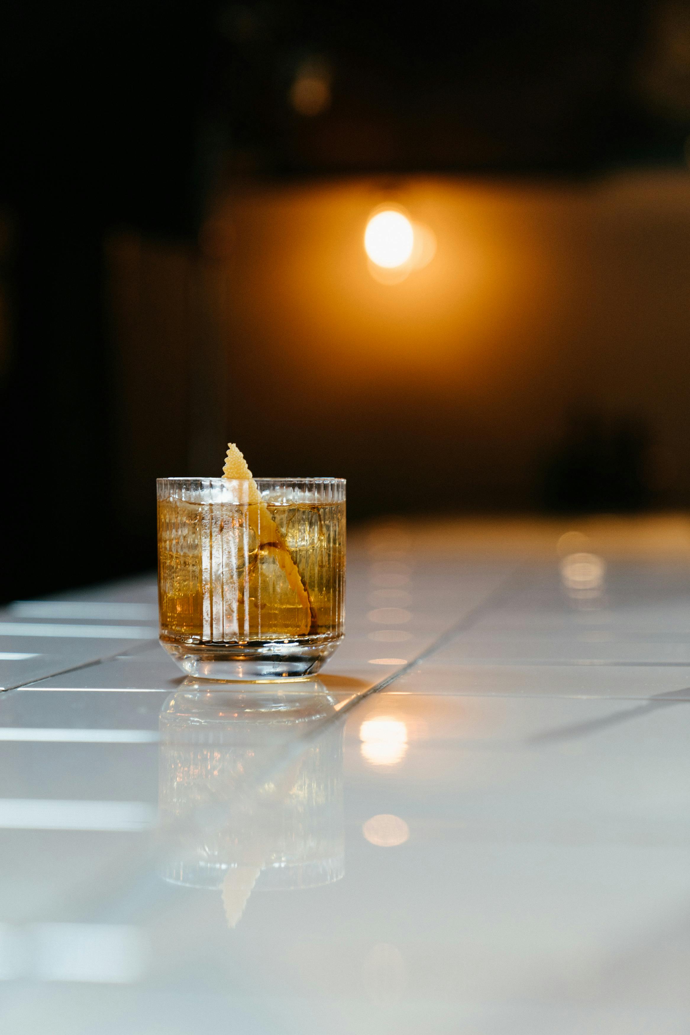Glass of whiskey with ice on bar counter.