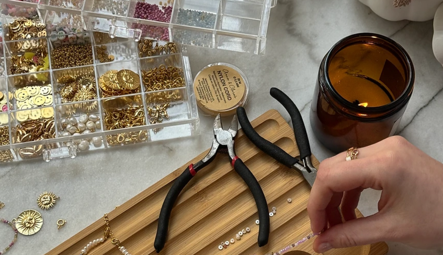 Hand fertigt Schmuck mit Perlen und Werkzeugen.