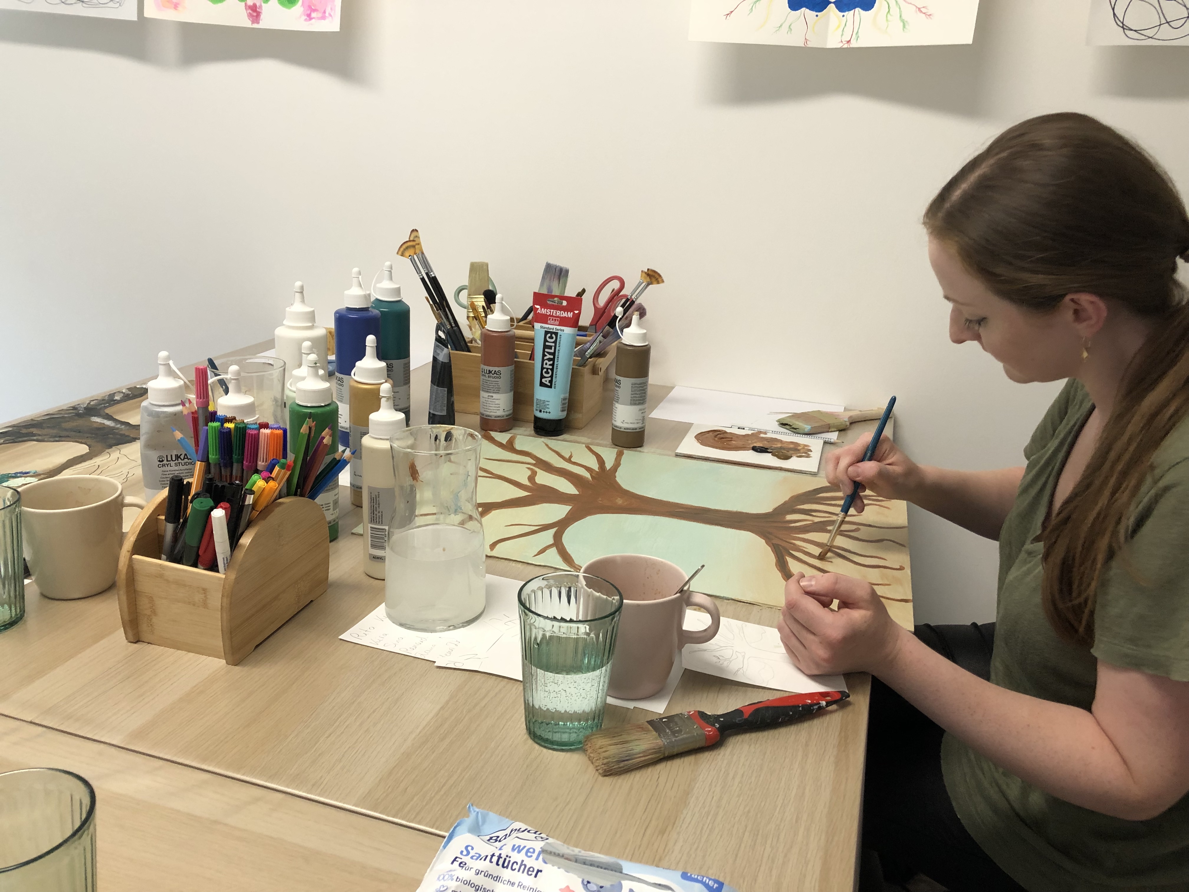 Woman painting tree at cluttered art desk.