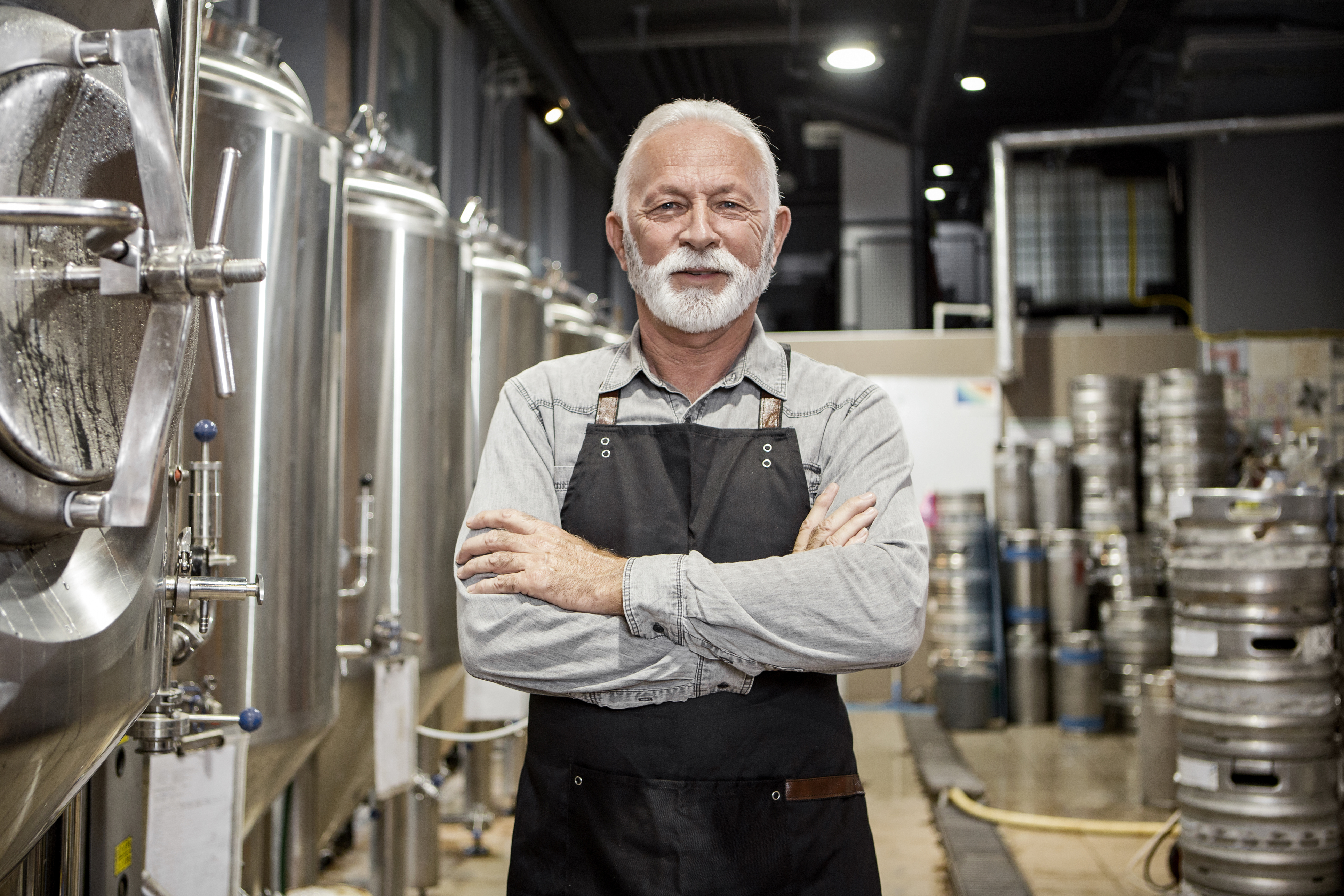 Mann mit Schürze steht in Brauerei mit Tanks.