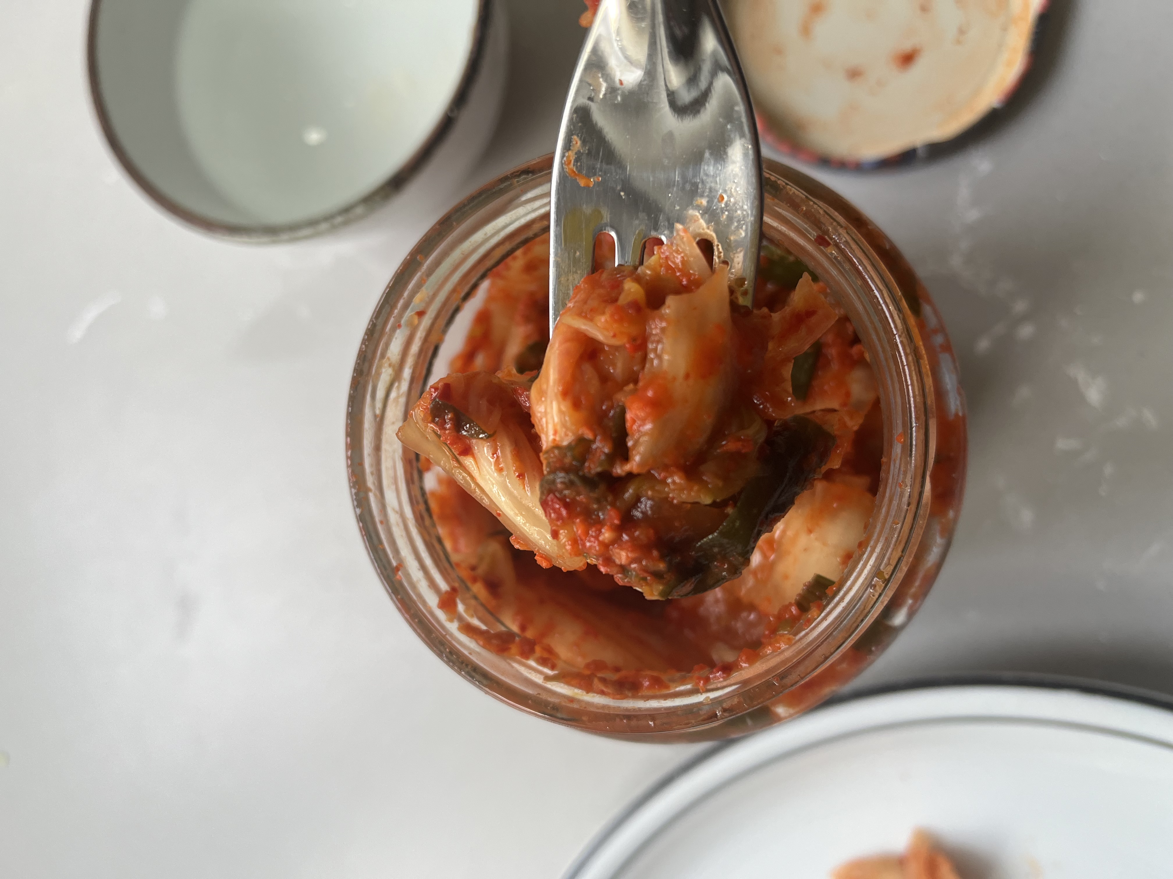 Fork holding kimchi above jar.
