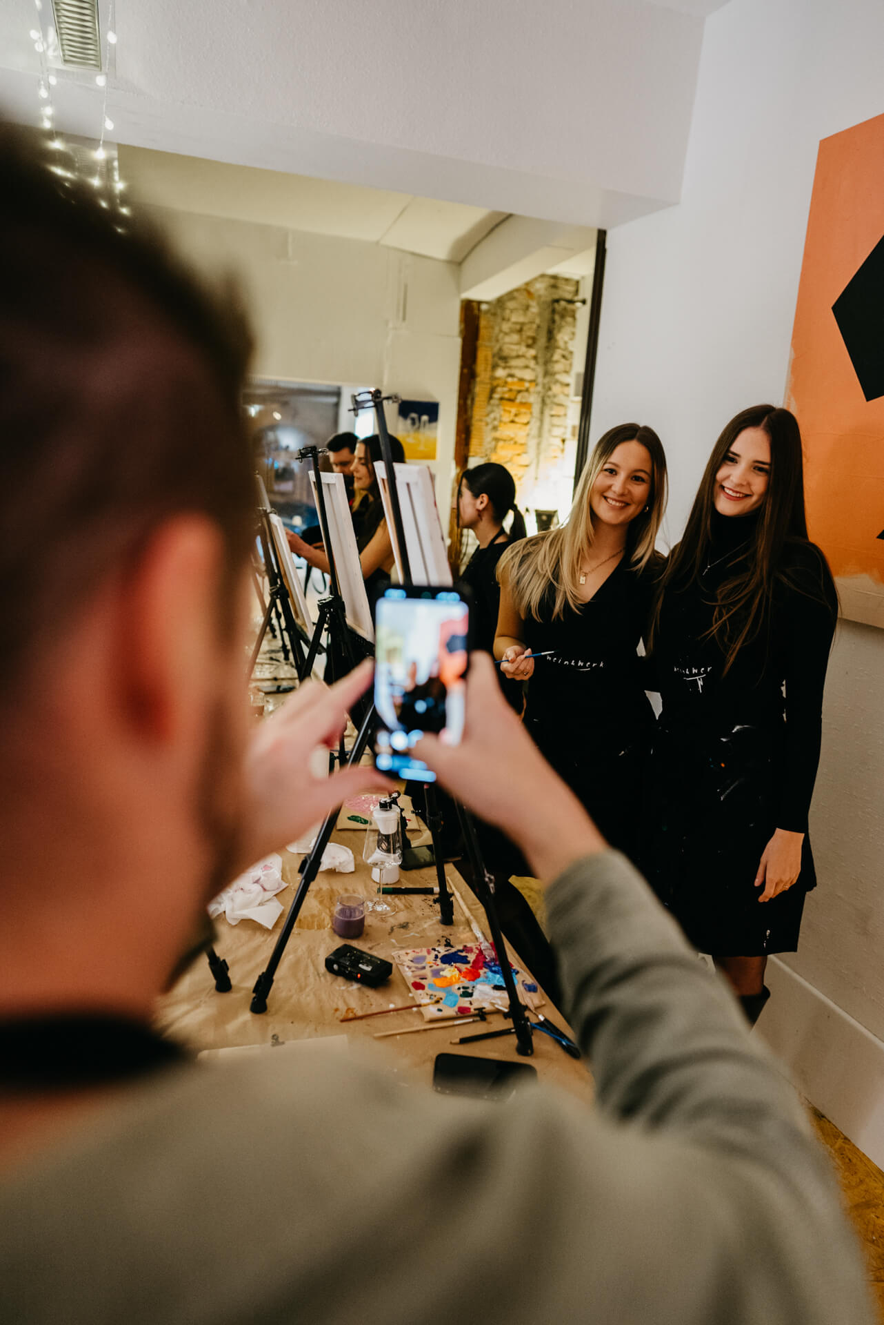 Two women posing, someone photographing with a phone.