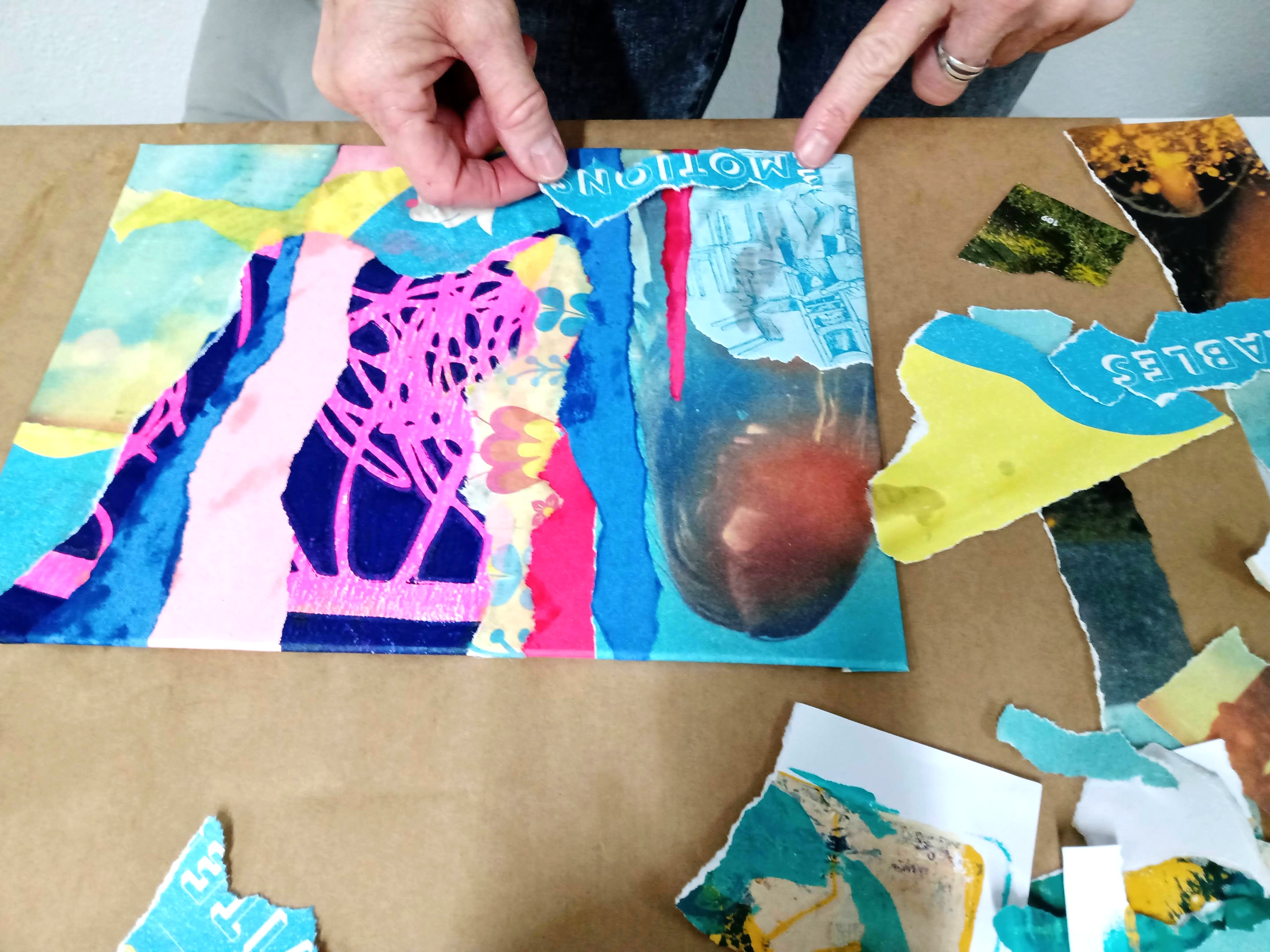 Person arranging colorful paper collage on table.
