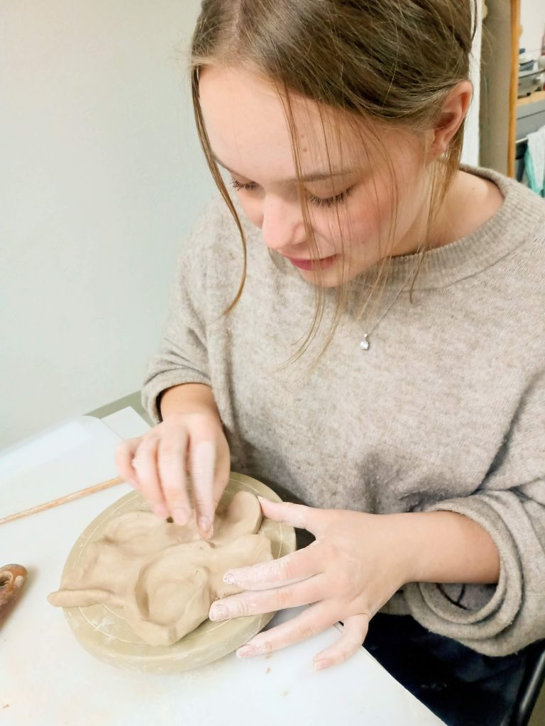 Woman sculpting clay on table indoors.