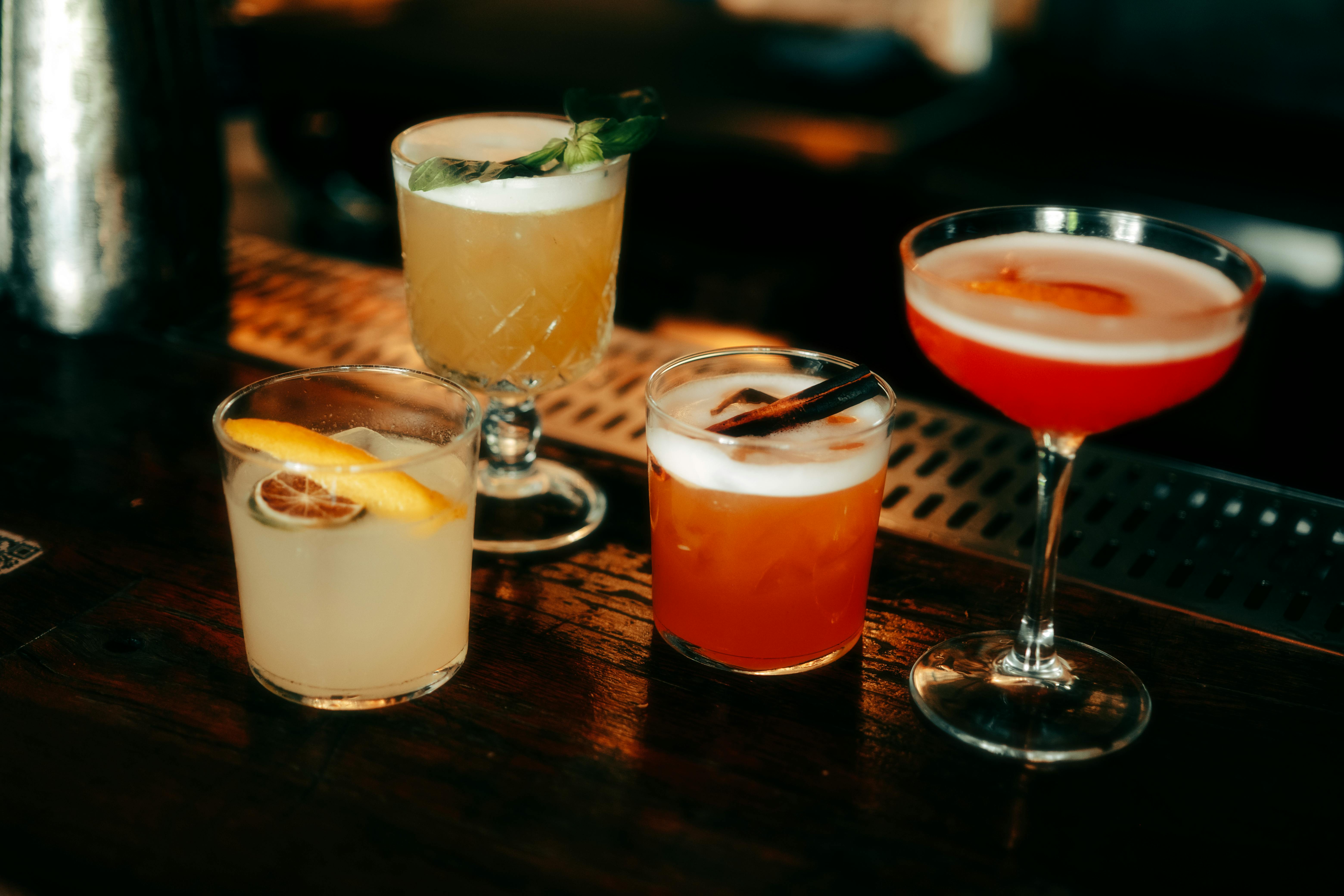 Vier bunte Cocktails auf einer Holztresen.