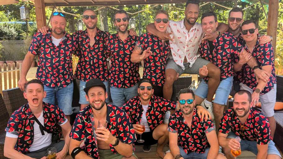 Group of men in matching shirts, outdoors, smiling.