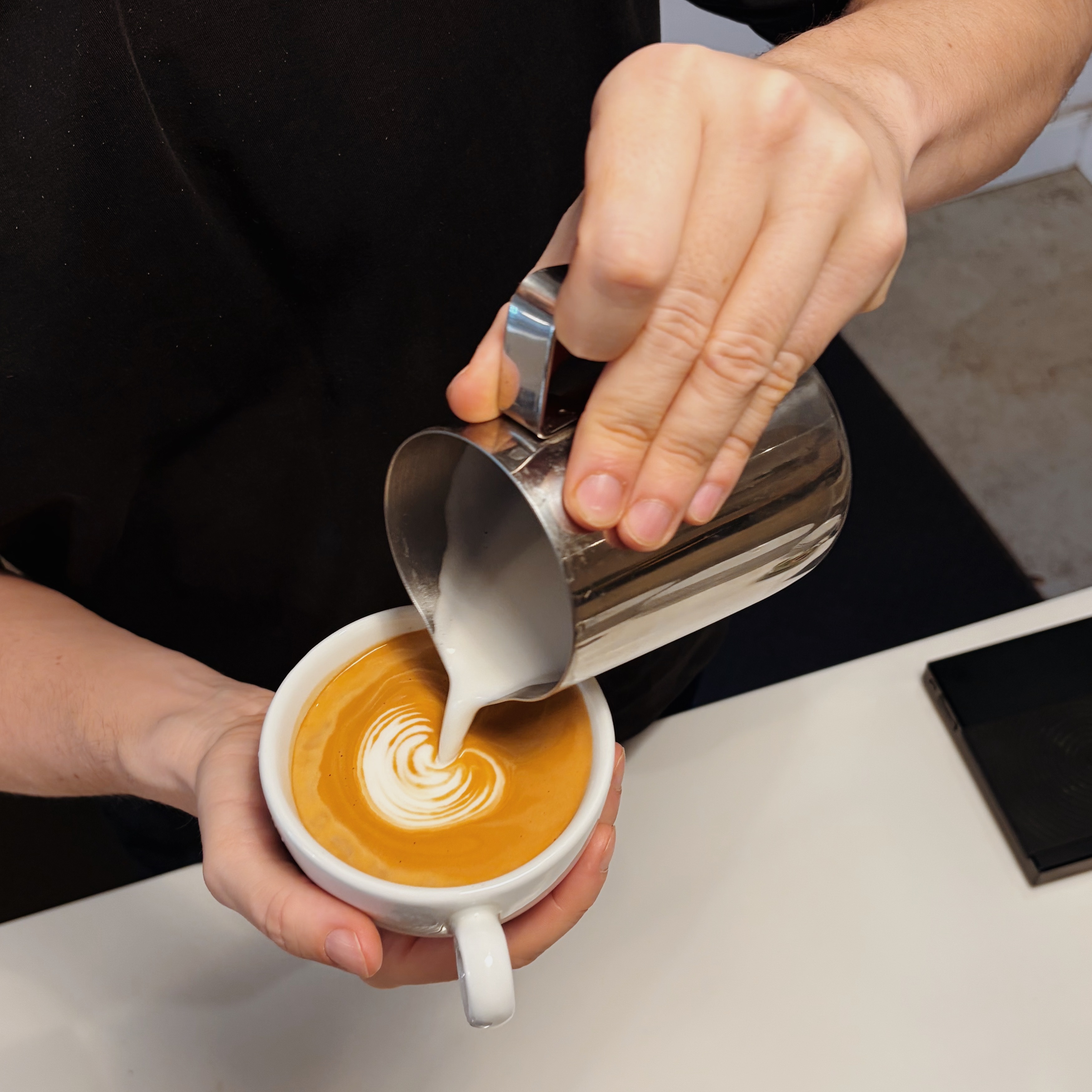 Barista gießt Milch und erstellt Latte Art.