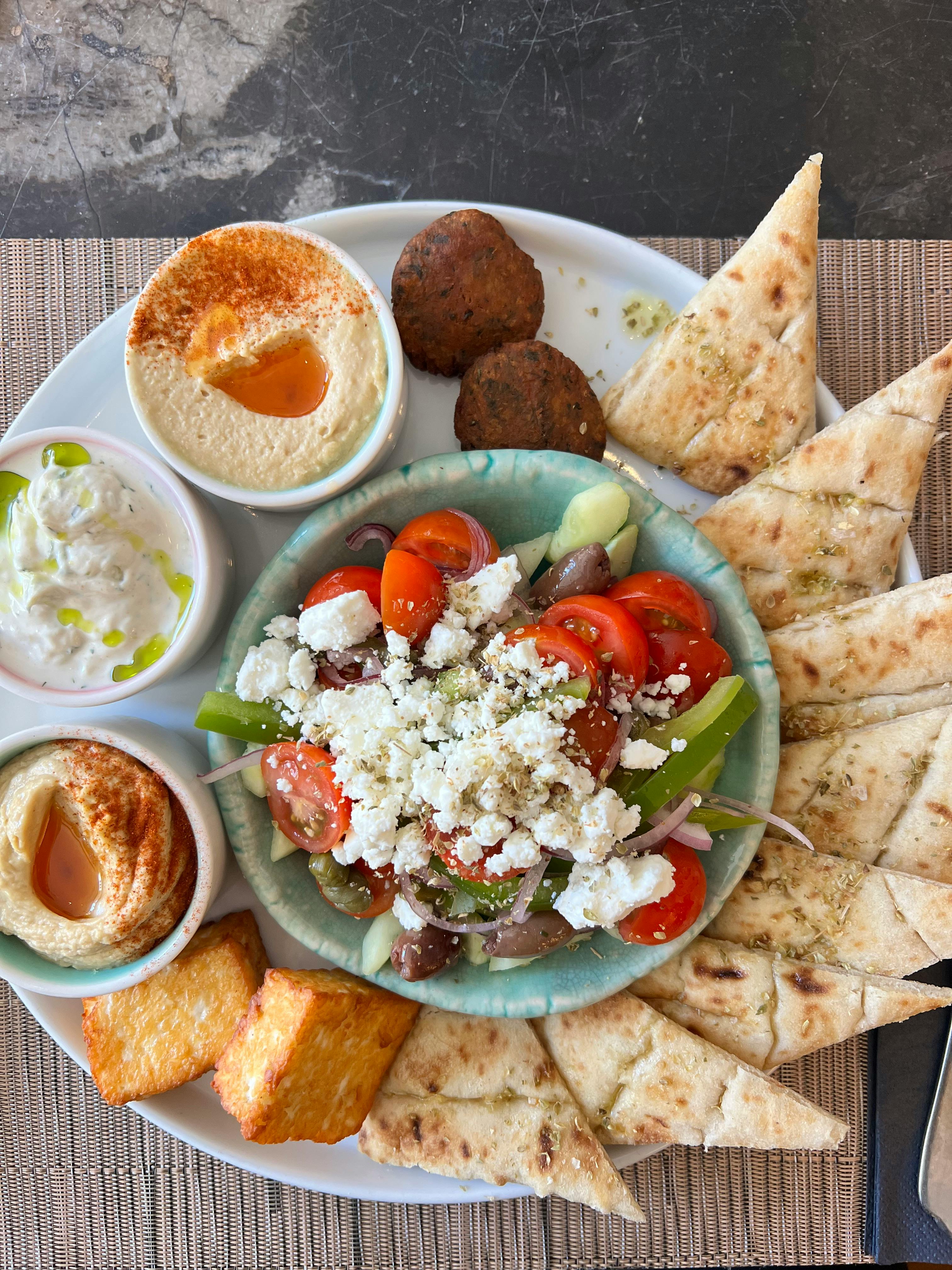 Greek salad surrounded by pita, hummus, and falafel.