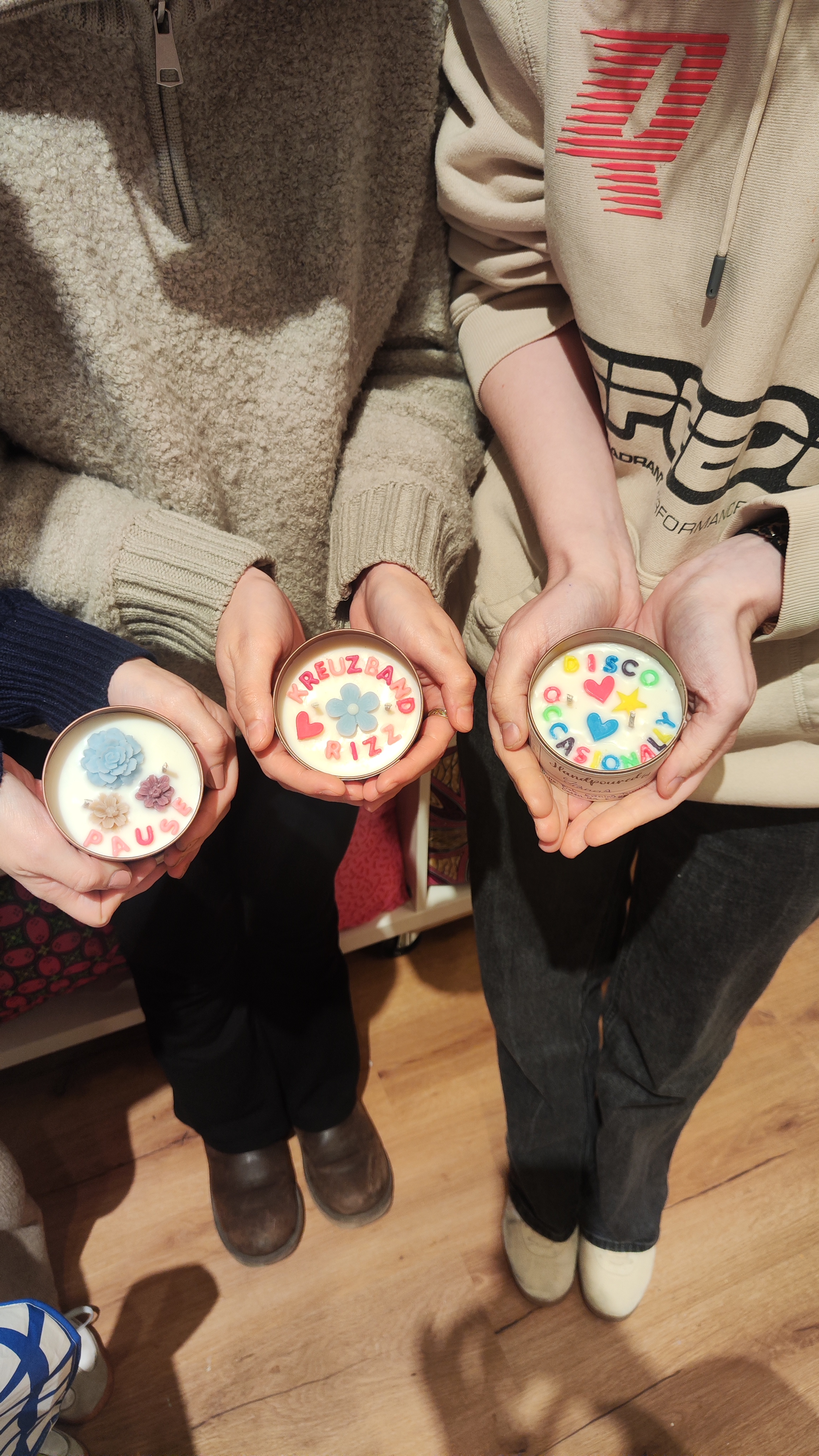 Three hands holding decorative candles indoors.