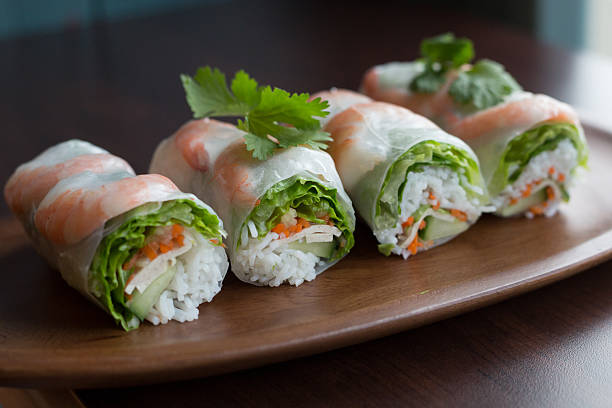 Fresh spring rolls lie on a brown wooden tray.