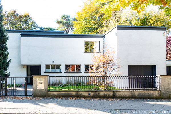 Modern white house with large windows, trees surrounding.