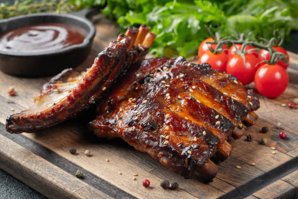 Grilled ribs lie on a wooden board with side dishes.