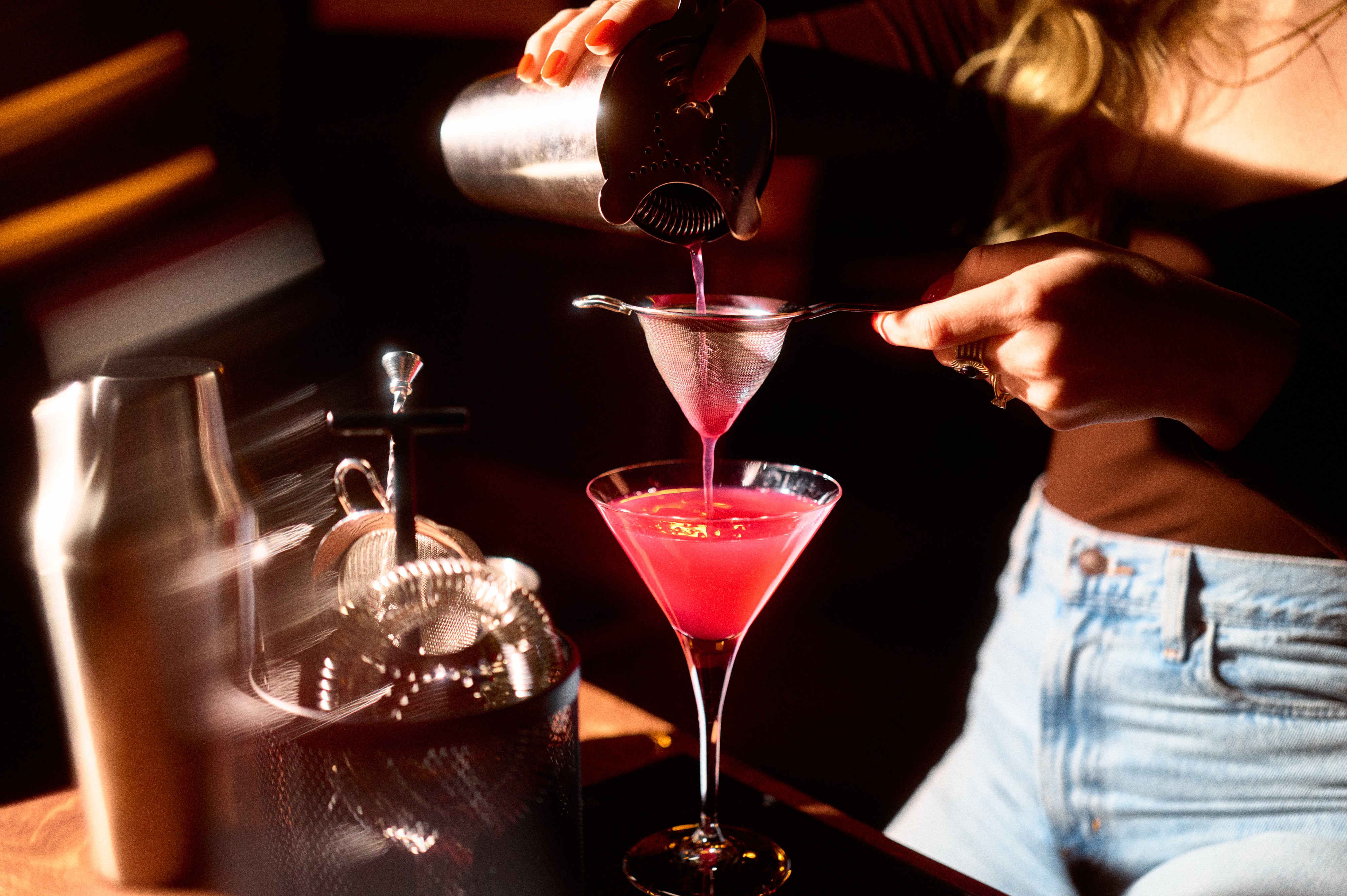 Person straining pink cocktail into glass.