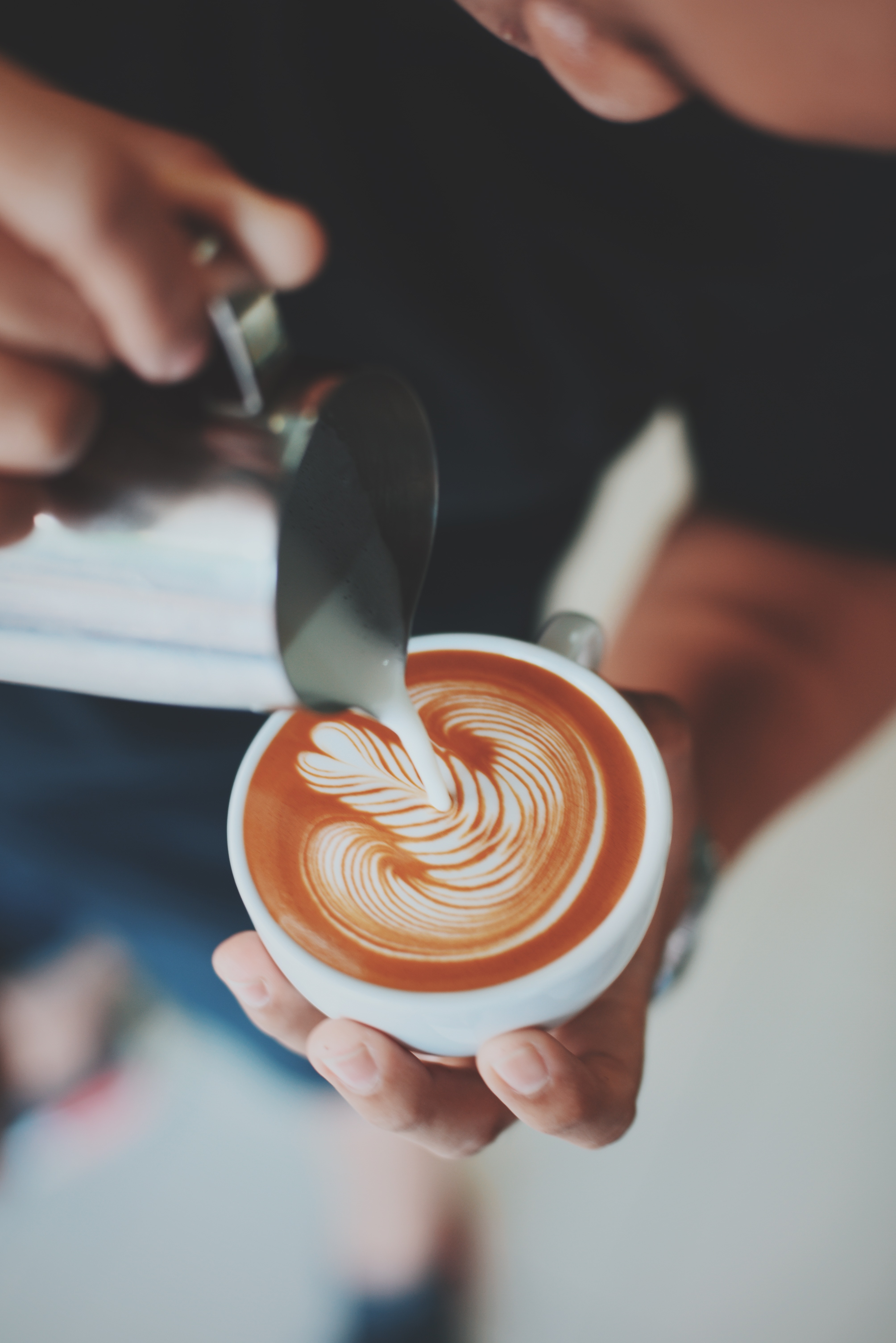 Cup of coffee is decorated with milk foam. Hands visible.