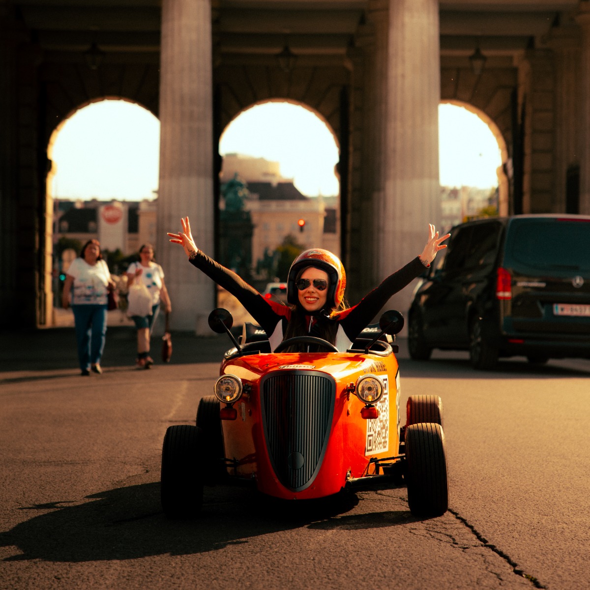 Person fährt freudig kleines oranges Auto draußen.