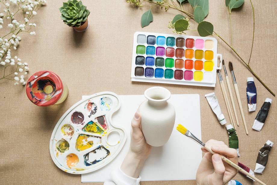 Hands painting vase on art table.