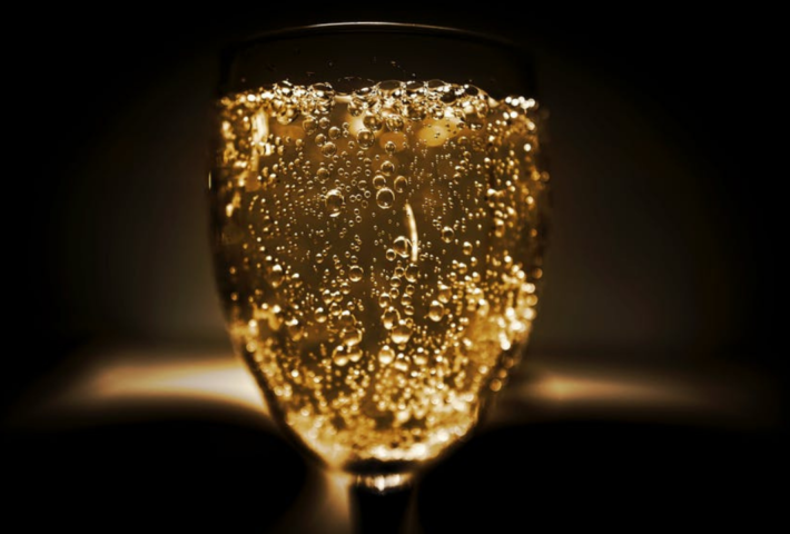 Ein Glas mit sprudelndem, goldenem Getränk in Dunkelheit.