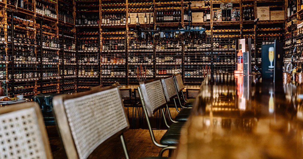 Bar counter facing extensive wine bottle shelves.