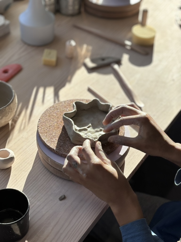 Hands shaping clay bowl on a wooden table.