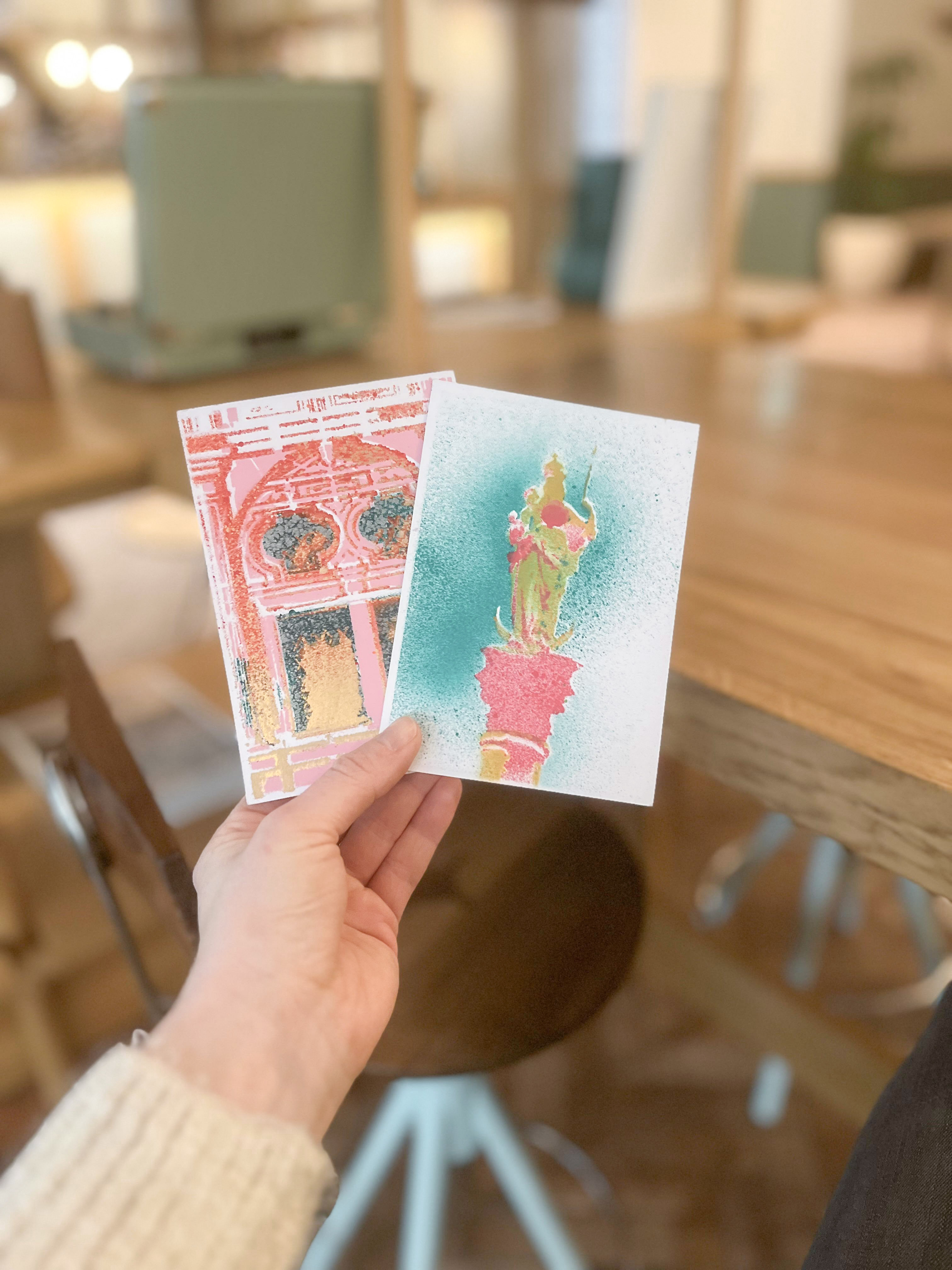 Hand holding two colorful postcards indoors.