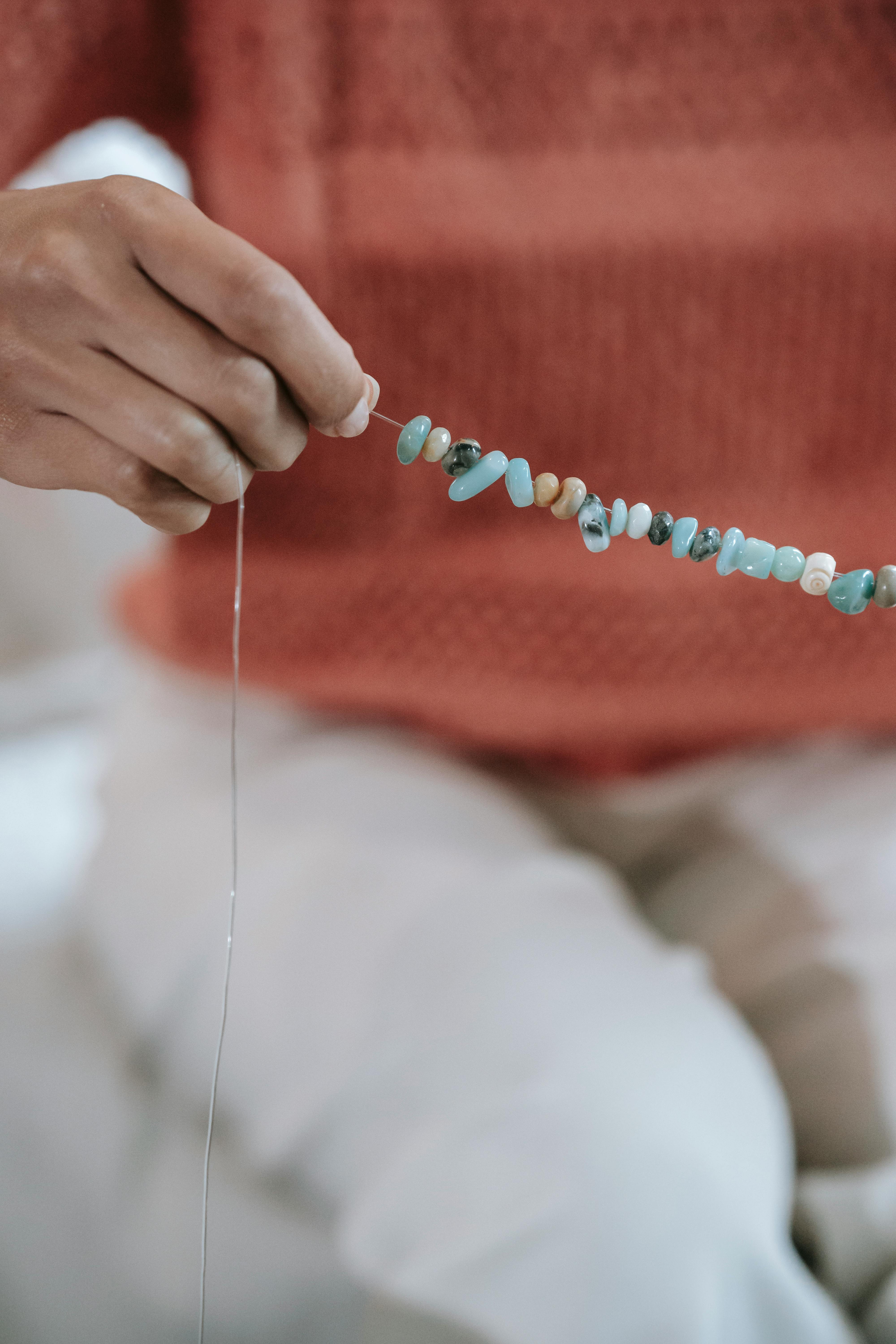 Hand threading beads on a string, indoor setting.
