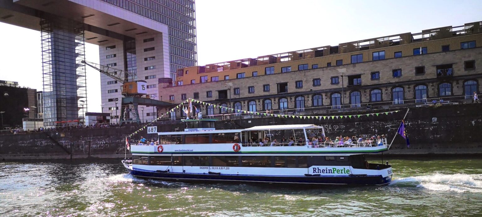 Boat sailing on river, industrial buildings nearby.