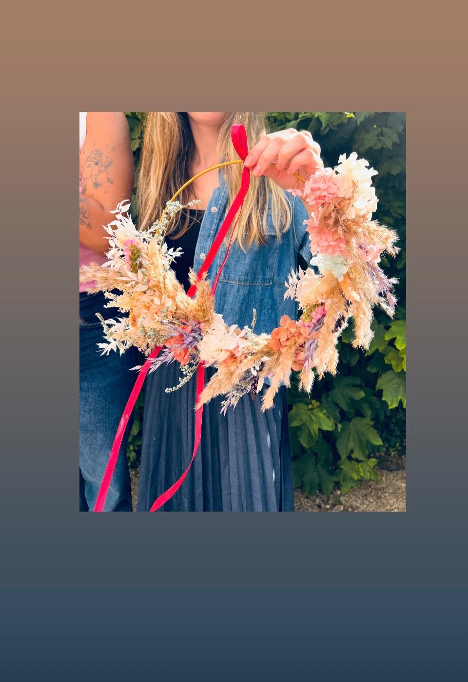 Person hält Blumenkranz mit rotem Band.
